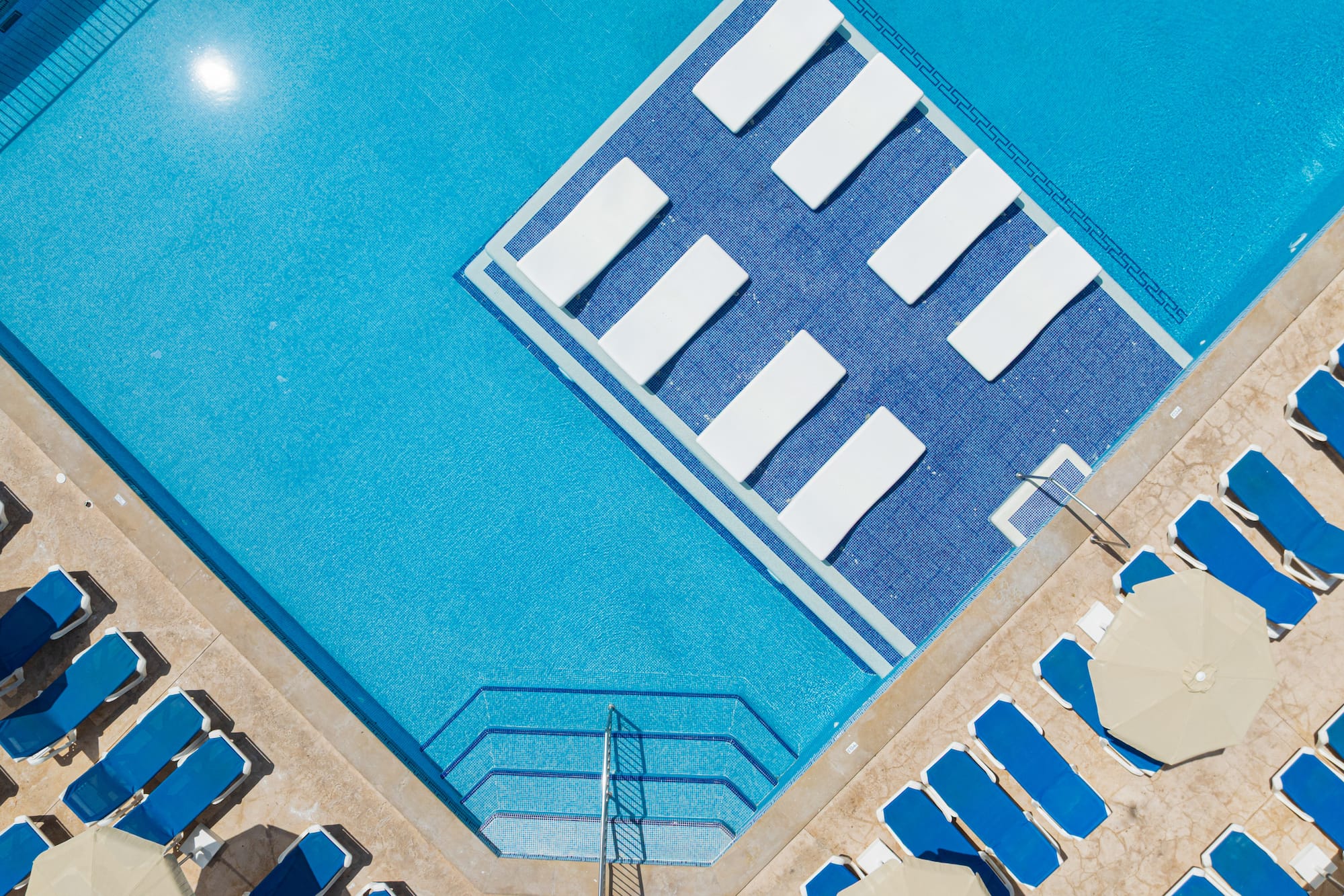 Aerial view: resort pool with blue water, in-pool loungers, and poolside chairs.