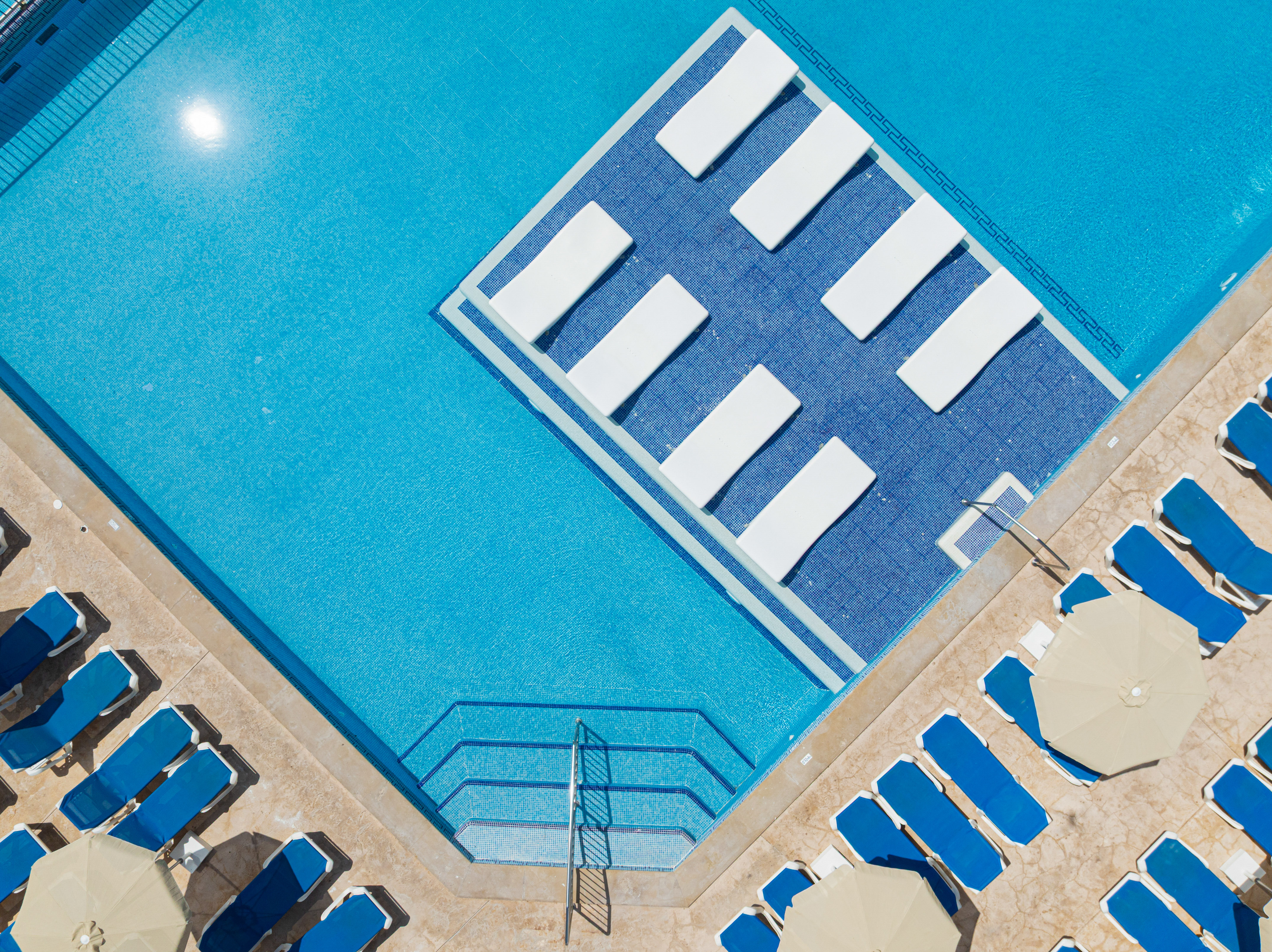 Aerial view bright blue resort swimming pool with sun loungers and umbrellas.
