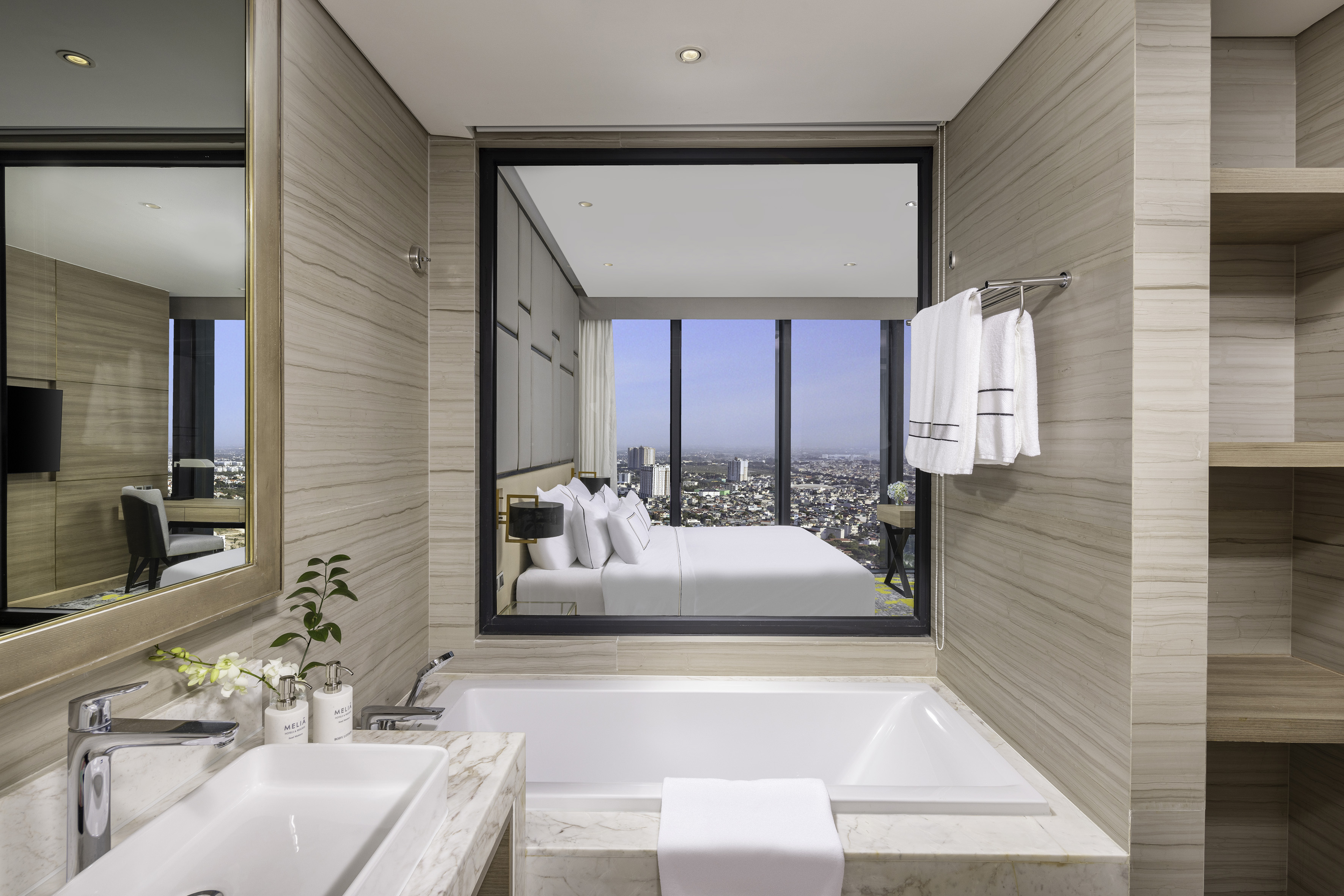 Luxury hotel bathroom with bathtub and bedroom city view.