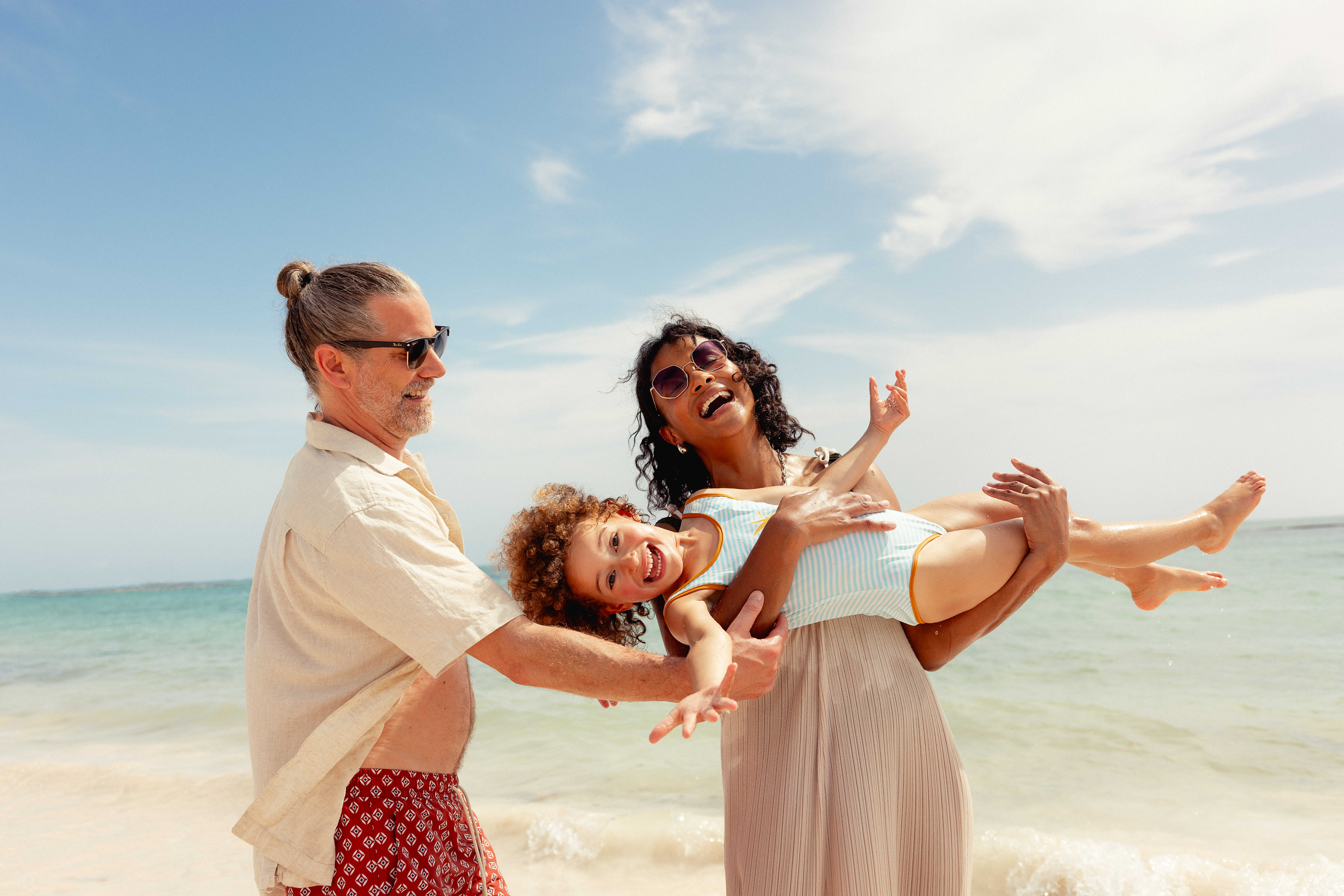 Happy family playing with laughing child on a sunny beach.