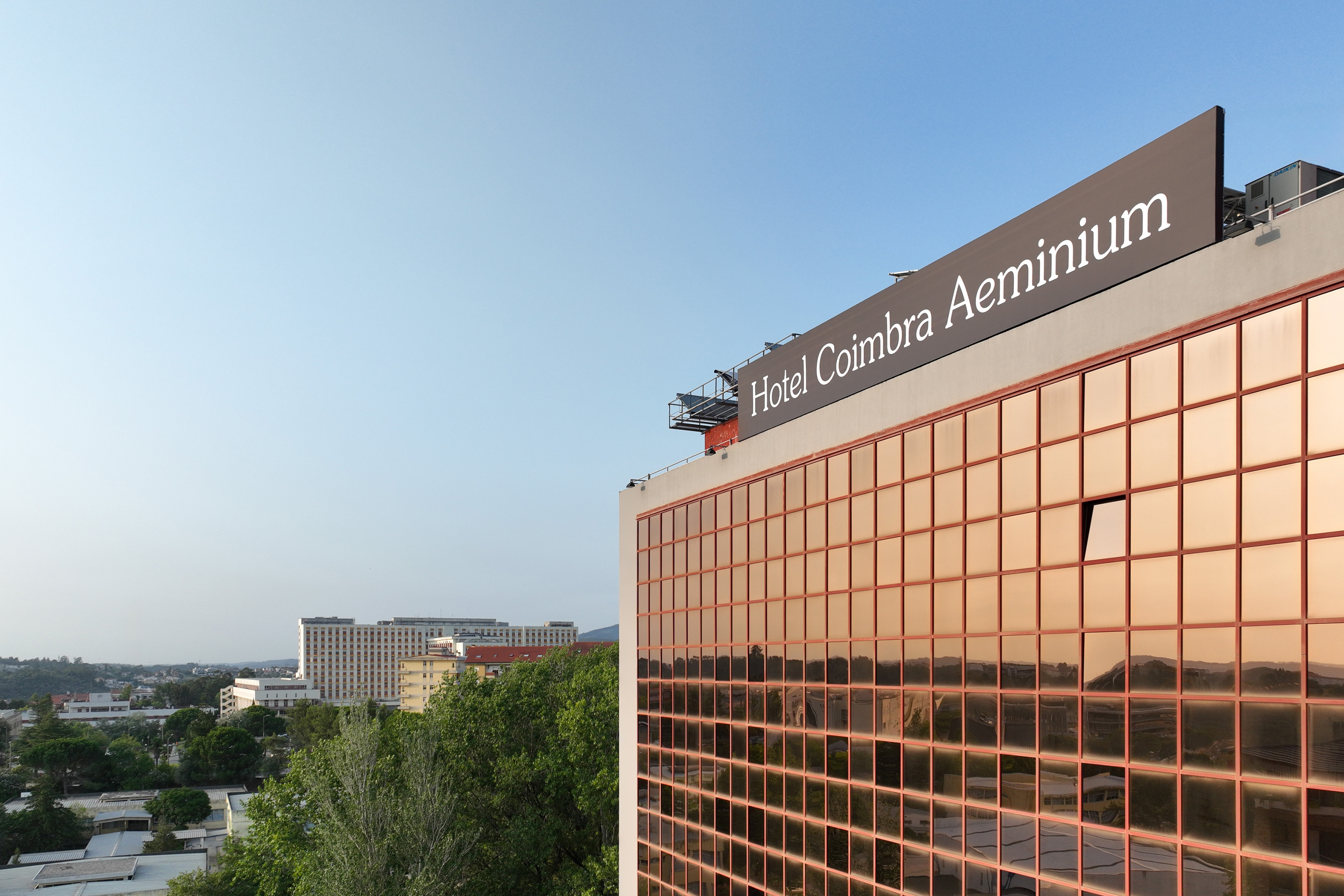 Hotel Coimbra Aeminium building with reflective golden windows, clear blue sky.