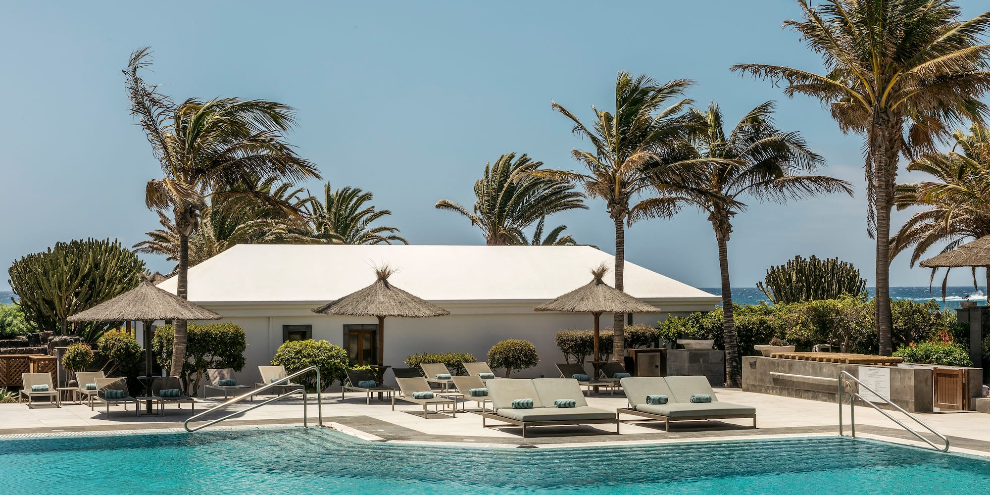 a pool with lounge chairs and umbrellas by a building