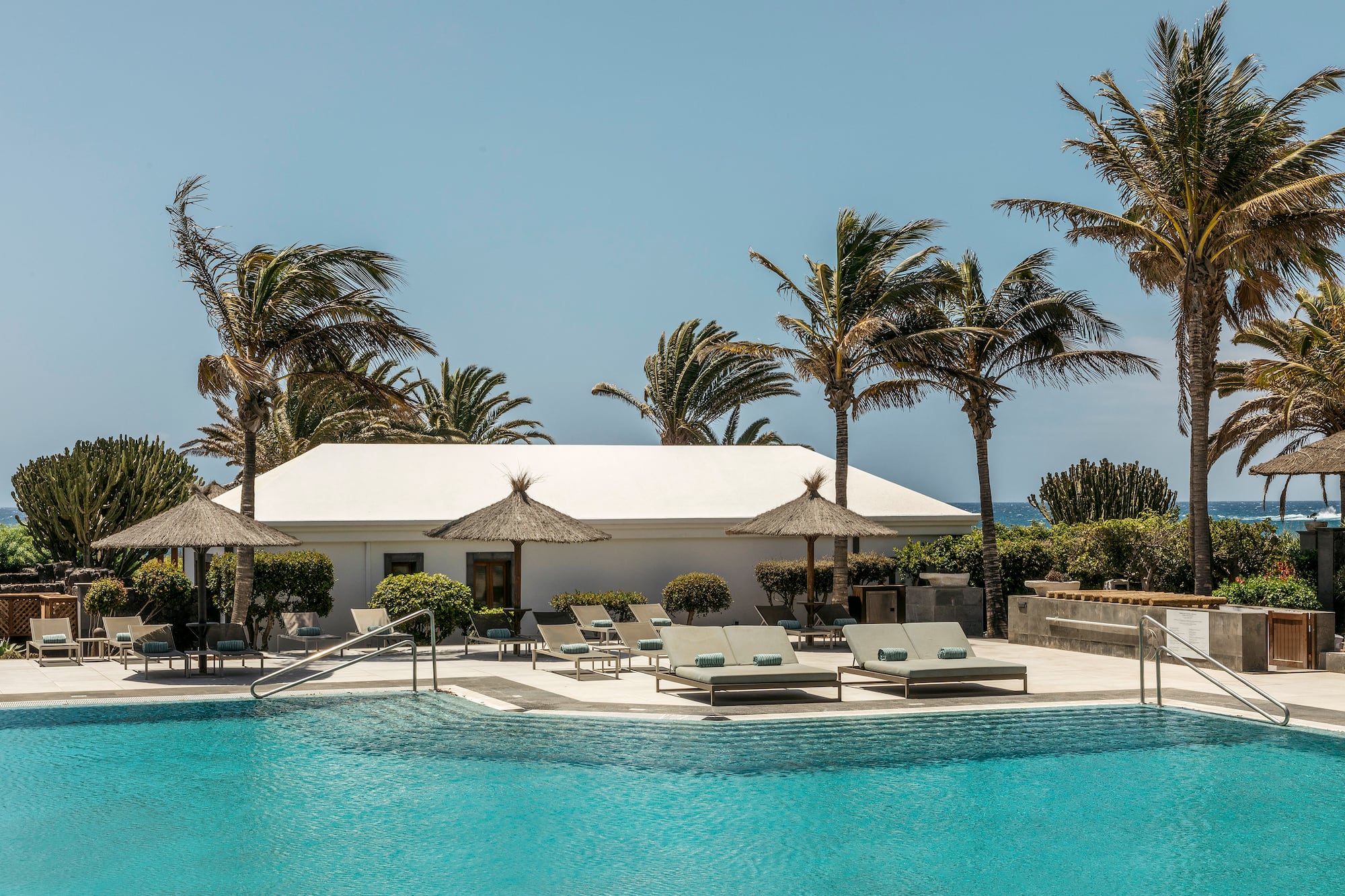 a pool with lounge chairs and umbrellas by a building