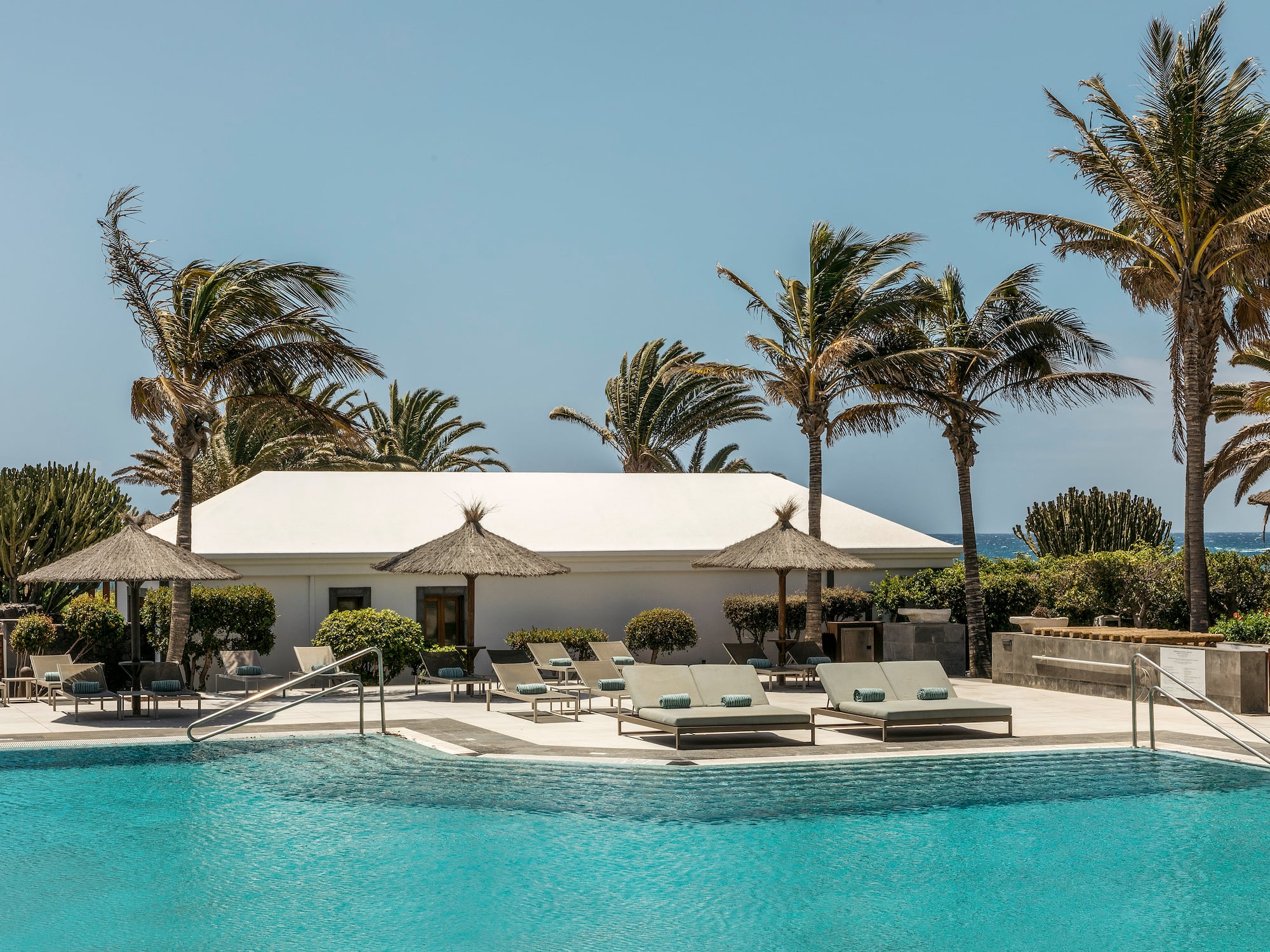 a pool with lounge chairs and umbrellas by a building