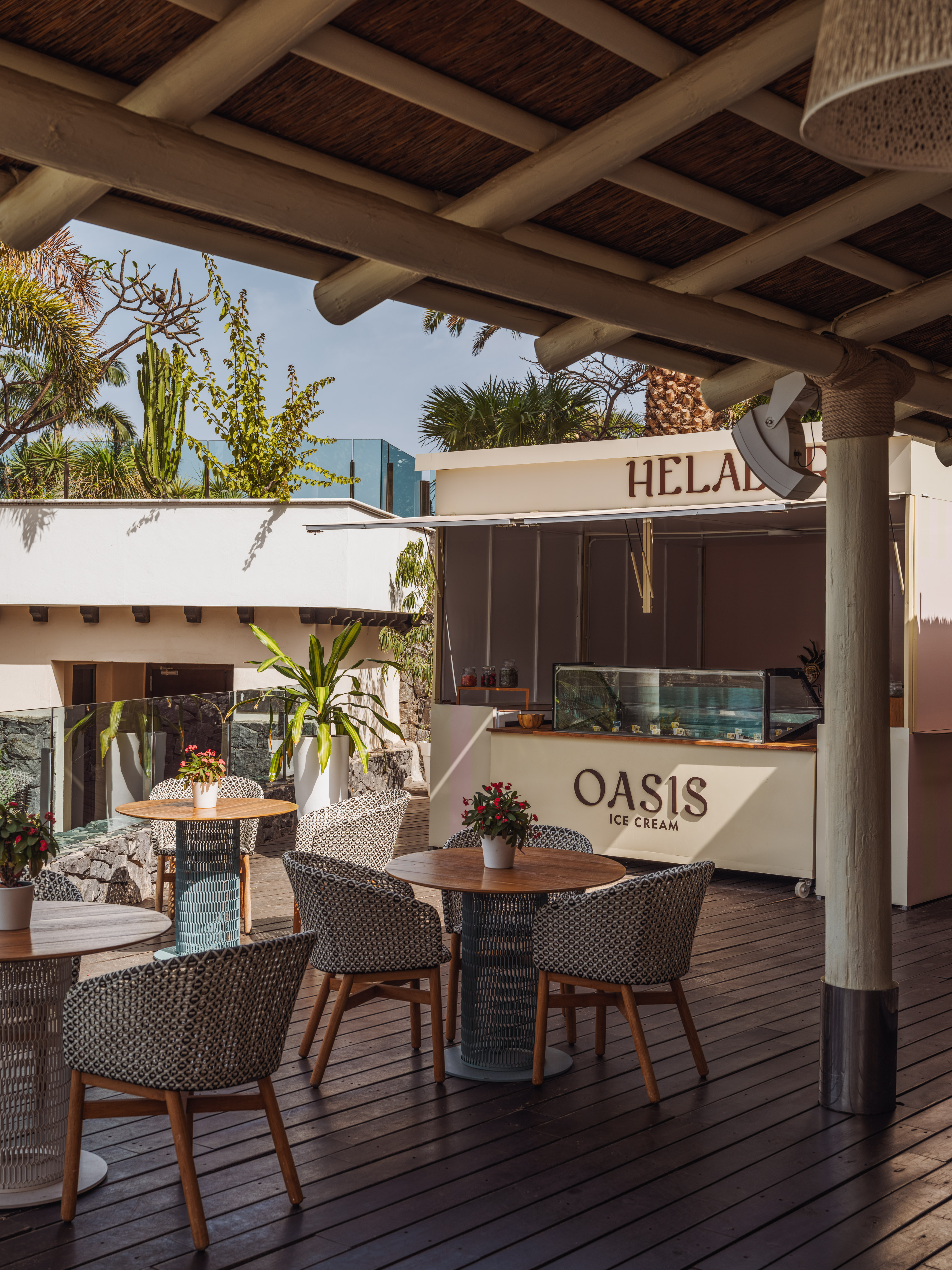 Oasis Ice Cream terrace, outdoor tables, woven chairs, tropical plants.