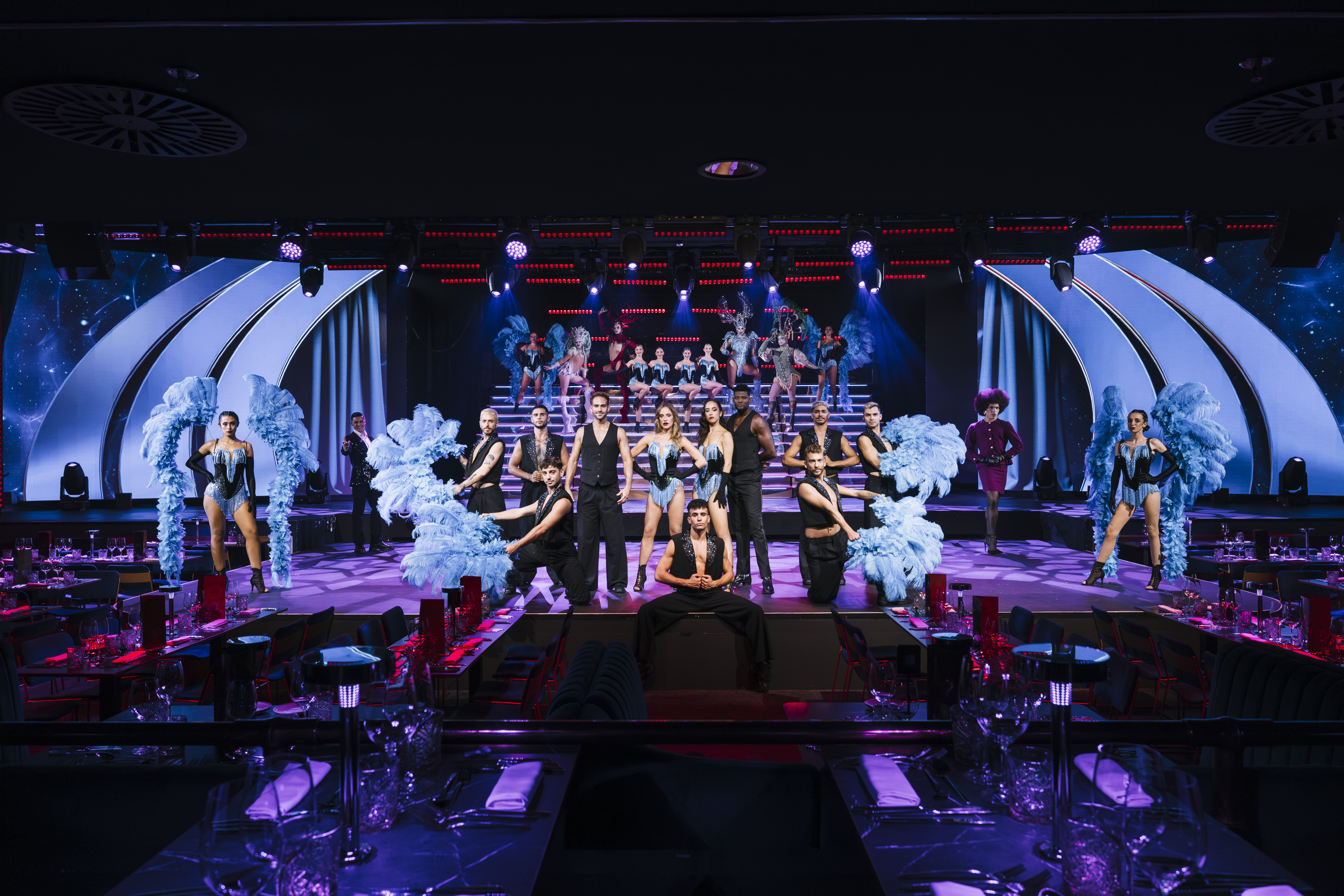 Cabaret show with performers in blue feather costumes on stage, dinner seating.