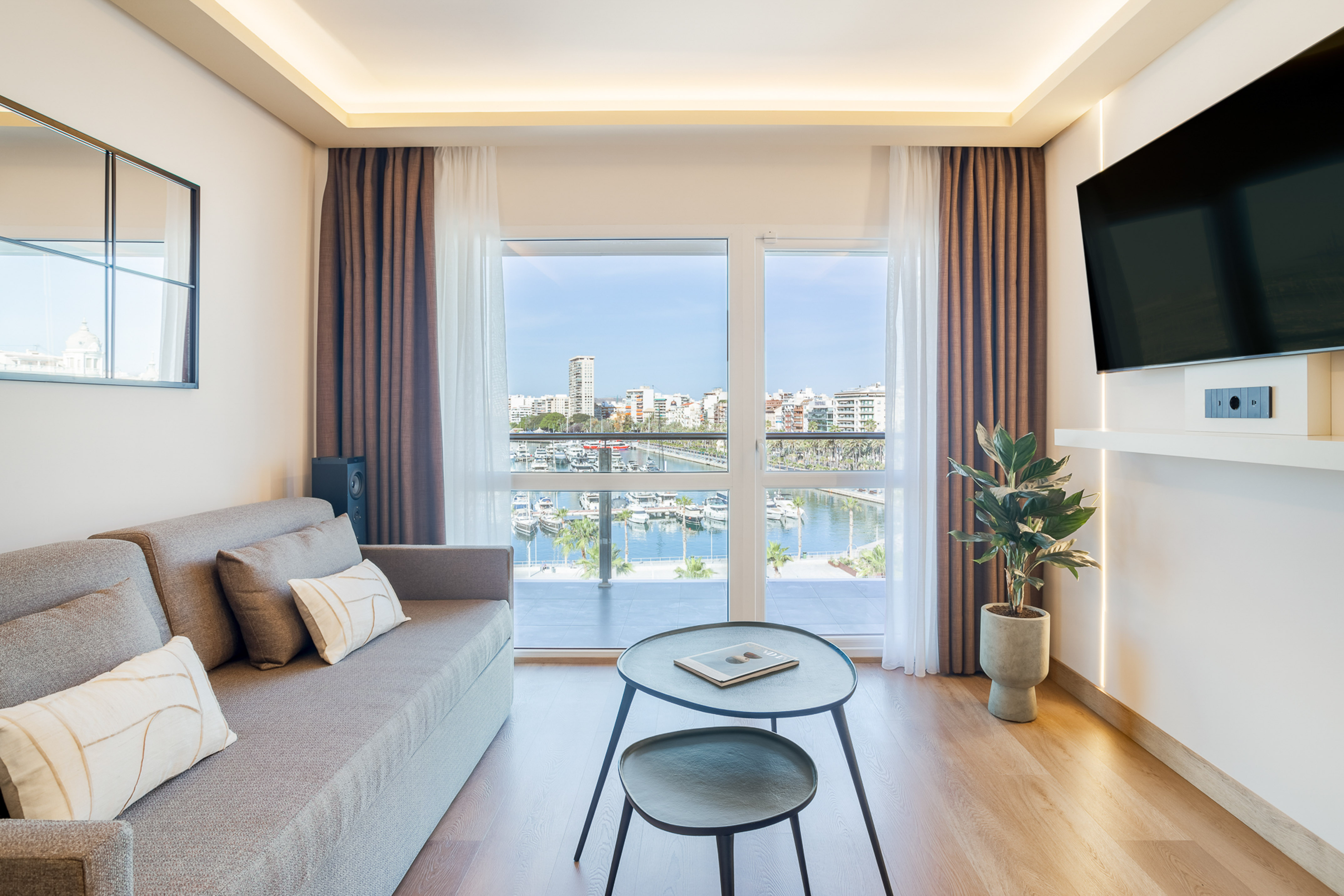 Waterfront living room with modern sofa, TV, and marina city view.