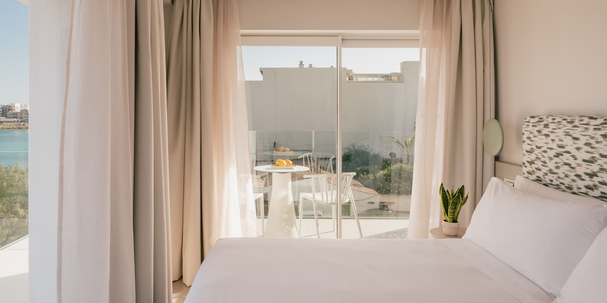 Modern hotel room with white bed, private balcony, and sea view.