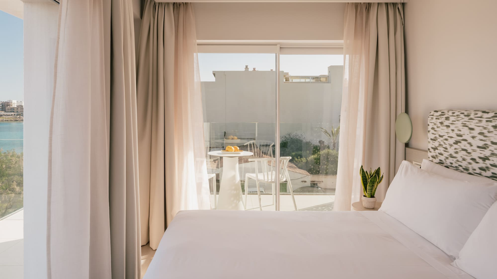 Modern hotel room with white bed, private balcony, and sea view.