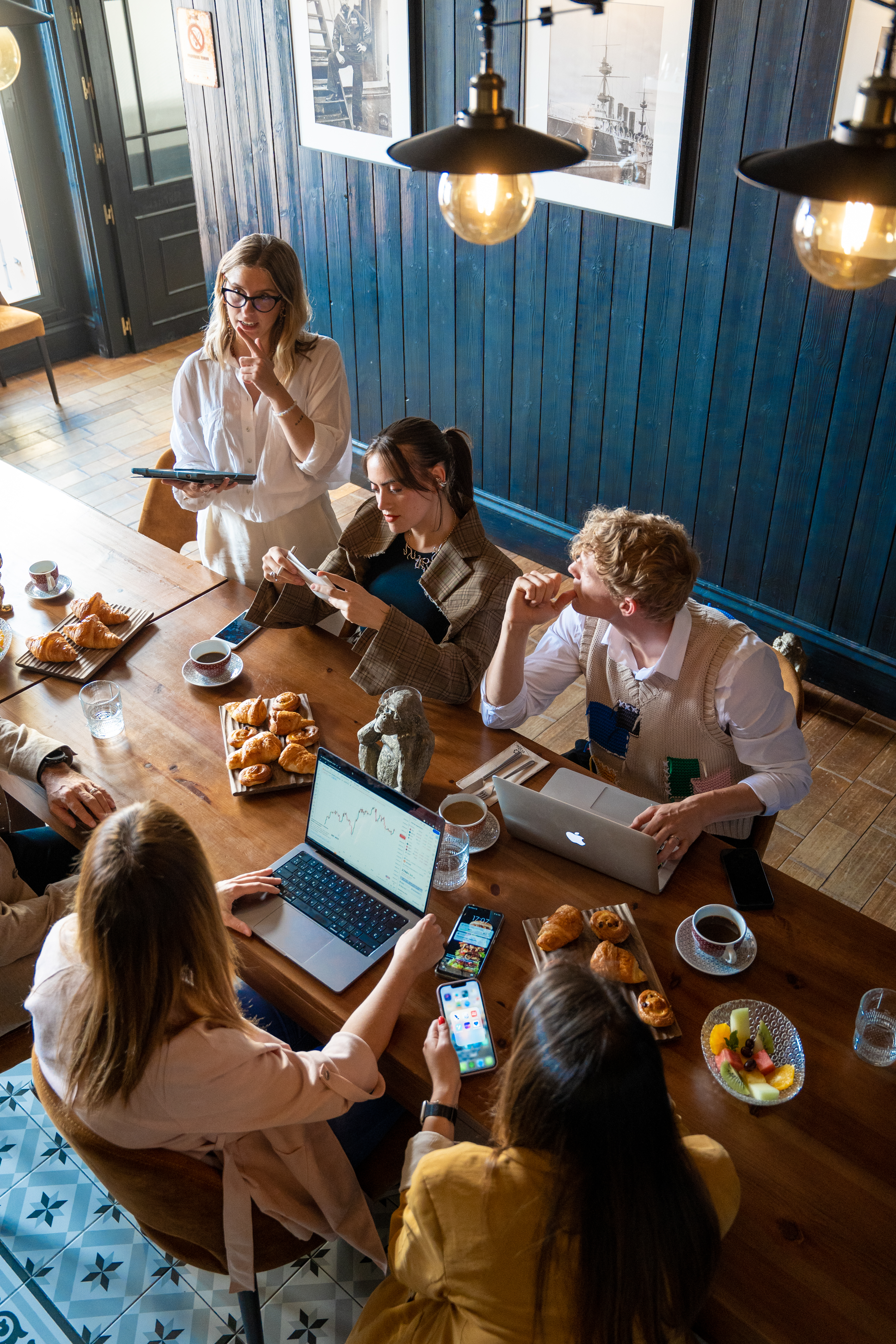 Diverse team collaborating at a cafe table with laptops, phones, and breakfast items.