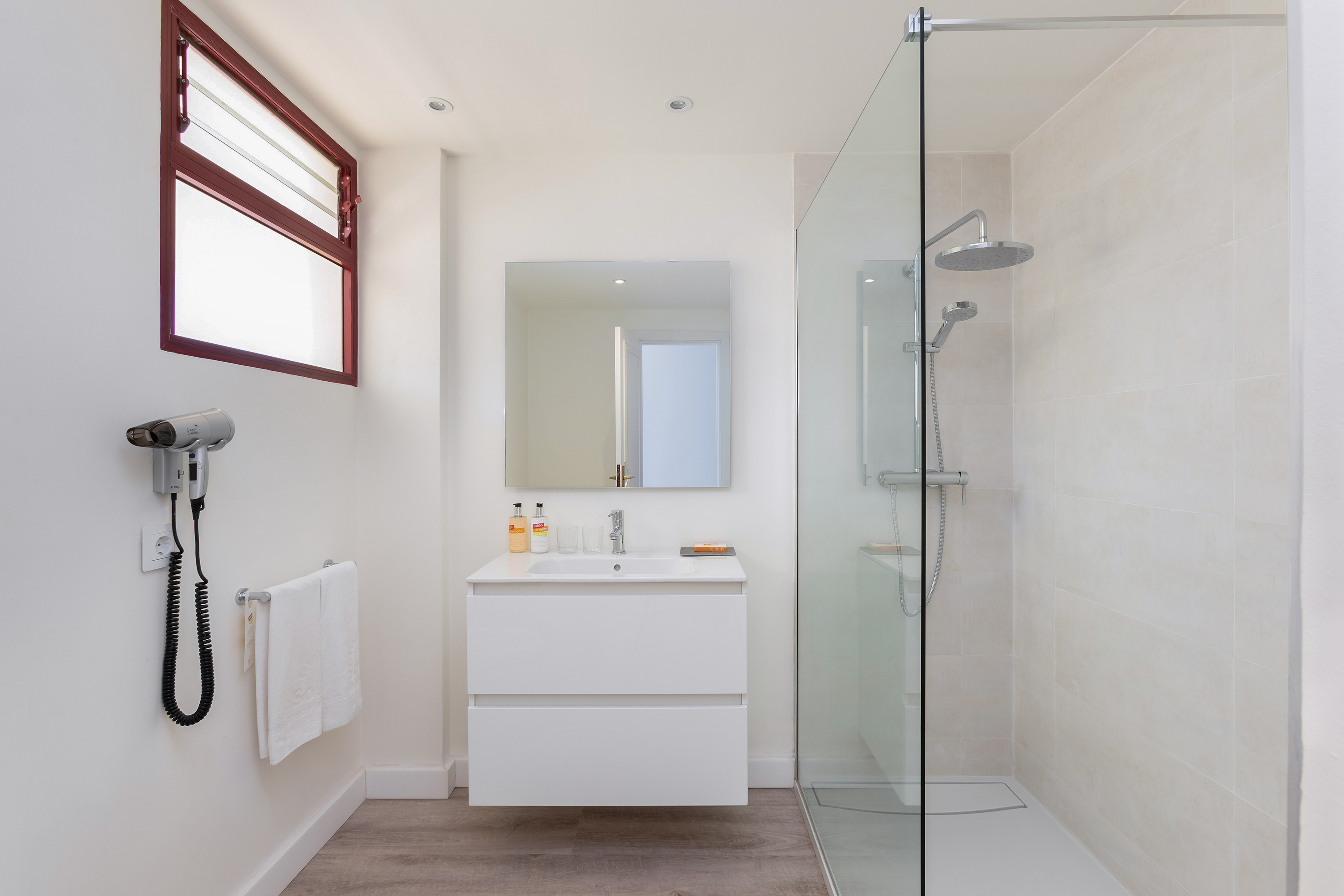 Modern bathroom with floating white vanity, glass shower, mirror, hairdryer.