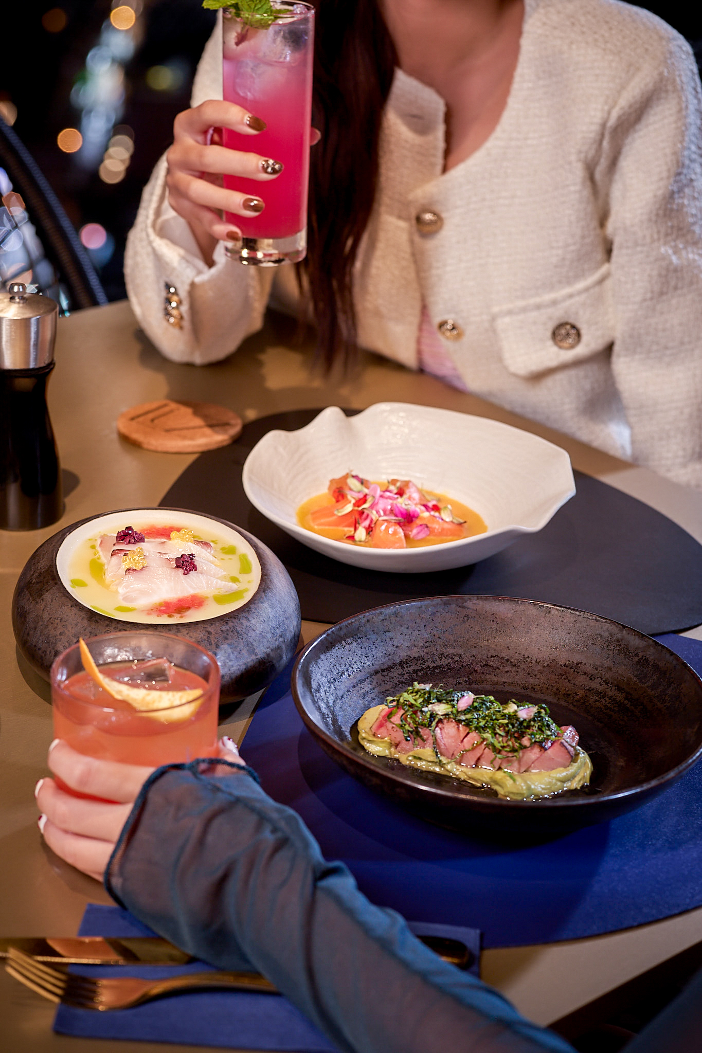 Two people enjoying gourmet appetizers, ceviche, and cocktails at a restaurant.