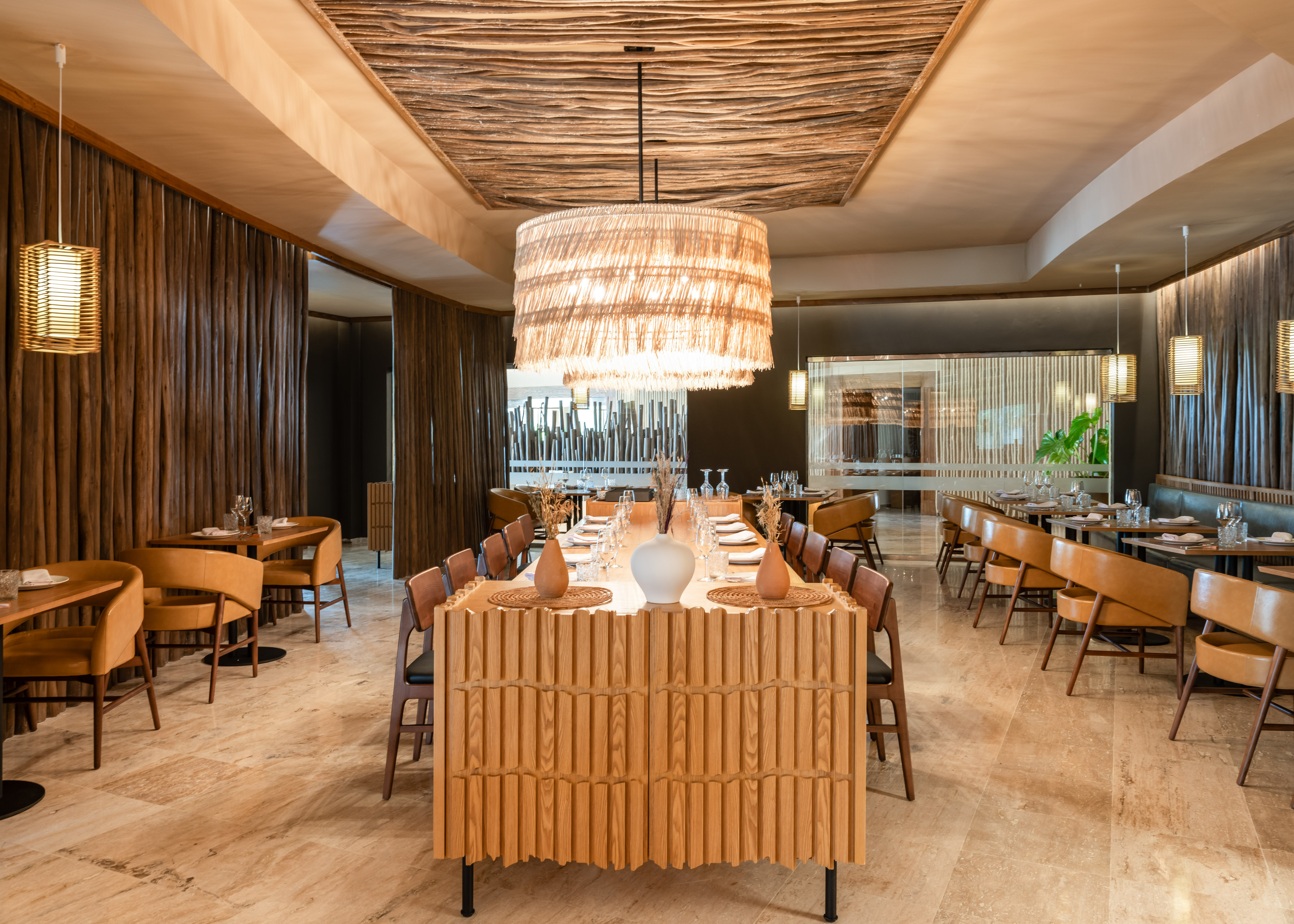 Modern restaurant with wood decor, large natural chandelier, and communal table.
