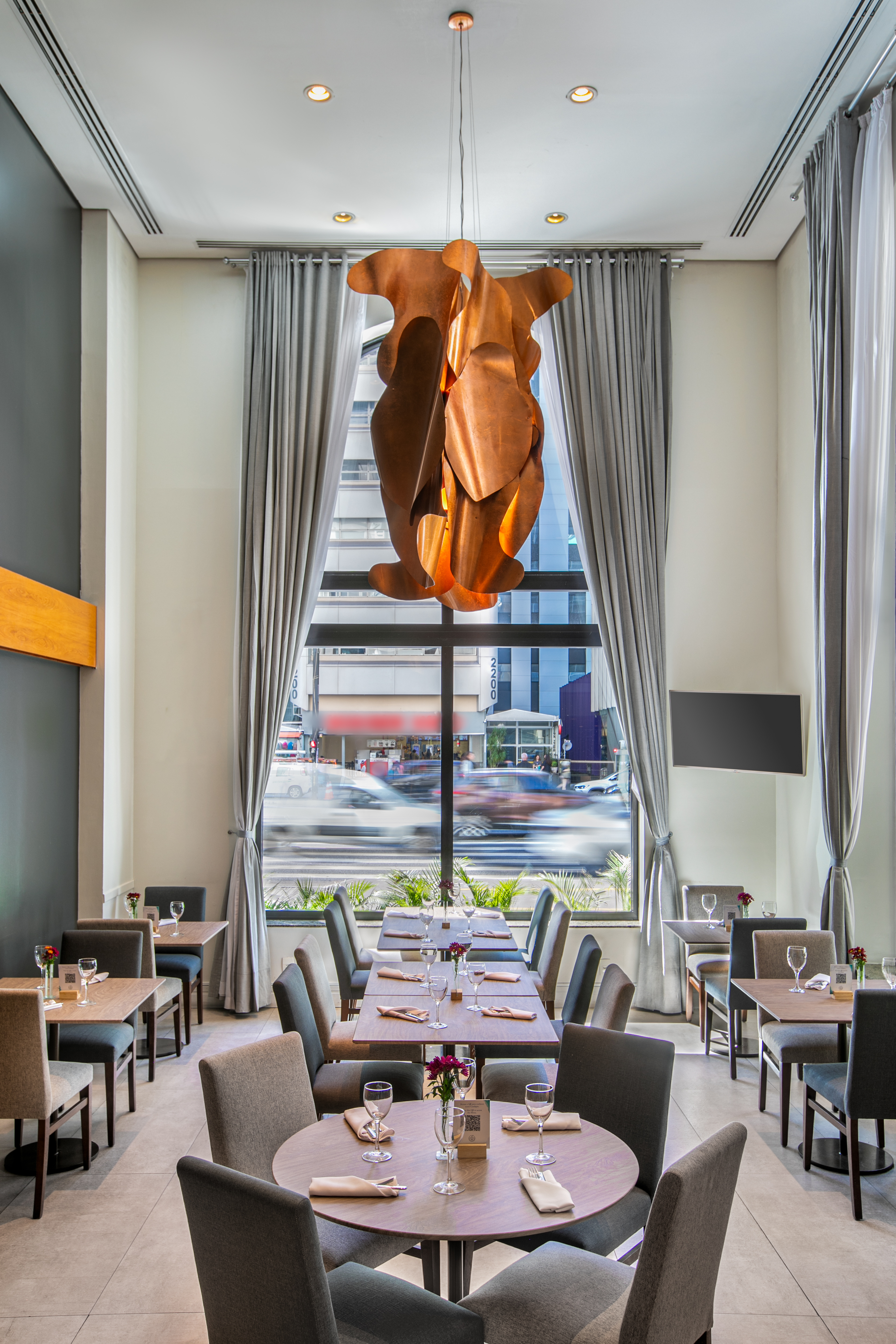 Modern restaurant dining room with city view, set tables, copper chandelier.