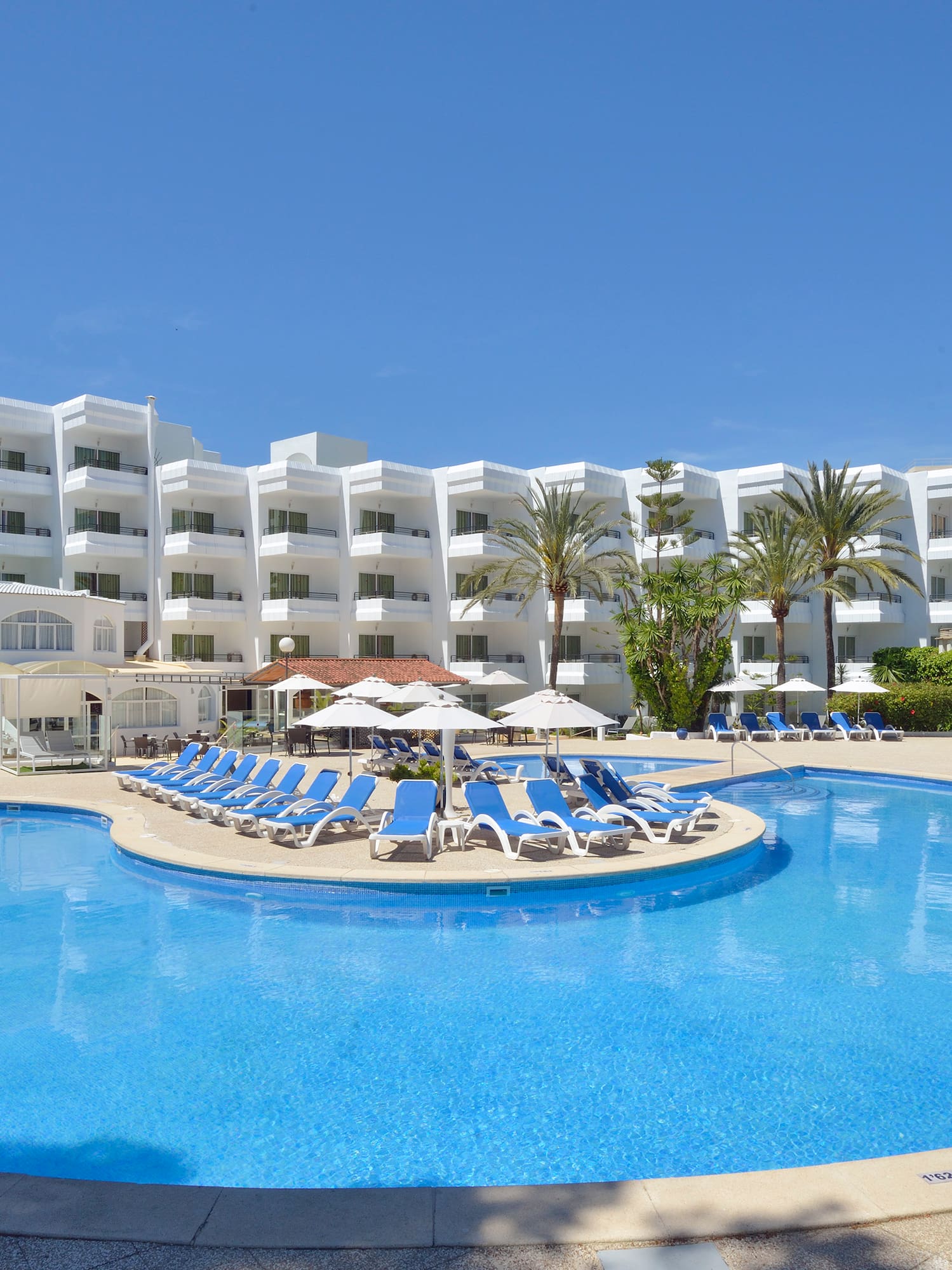 a pool with lounge chairs and umbrellas in front of a hotel