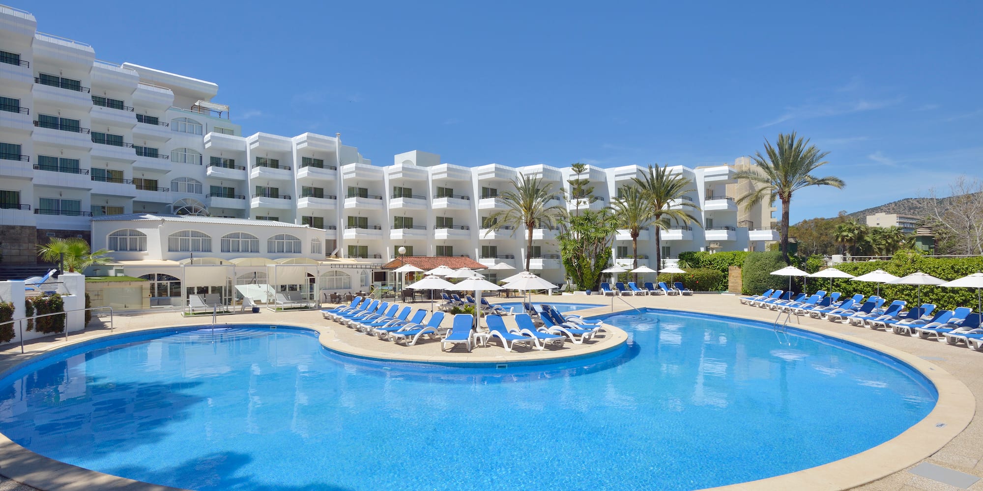 a pool with lounge chairs and umbrellas in front of a hotel