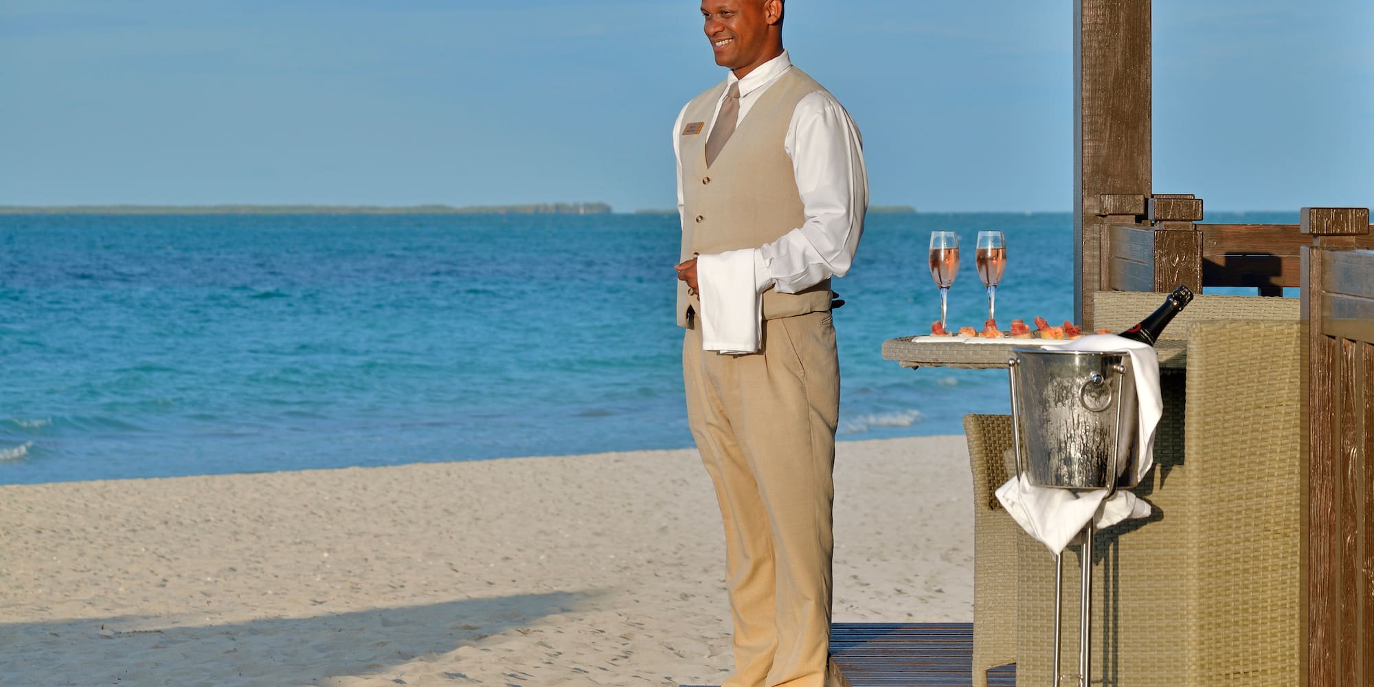 a man standing on a deck with a tray of wine and a tray of food