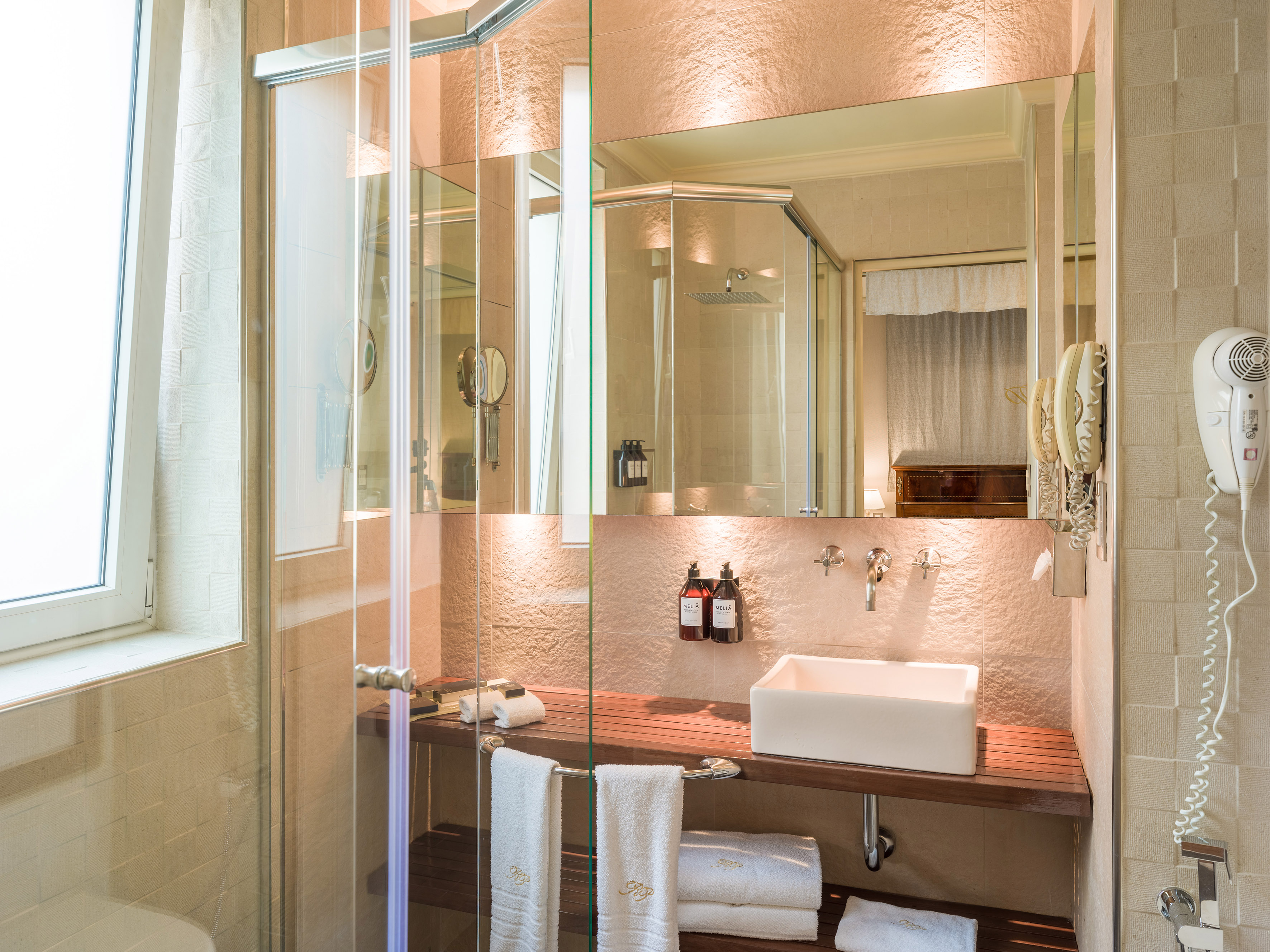 Modern bathroom with glass shower, wooden vanity, white sink, and clean towels.