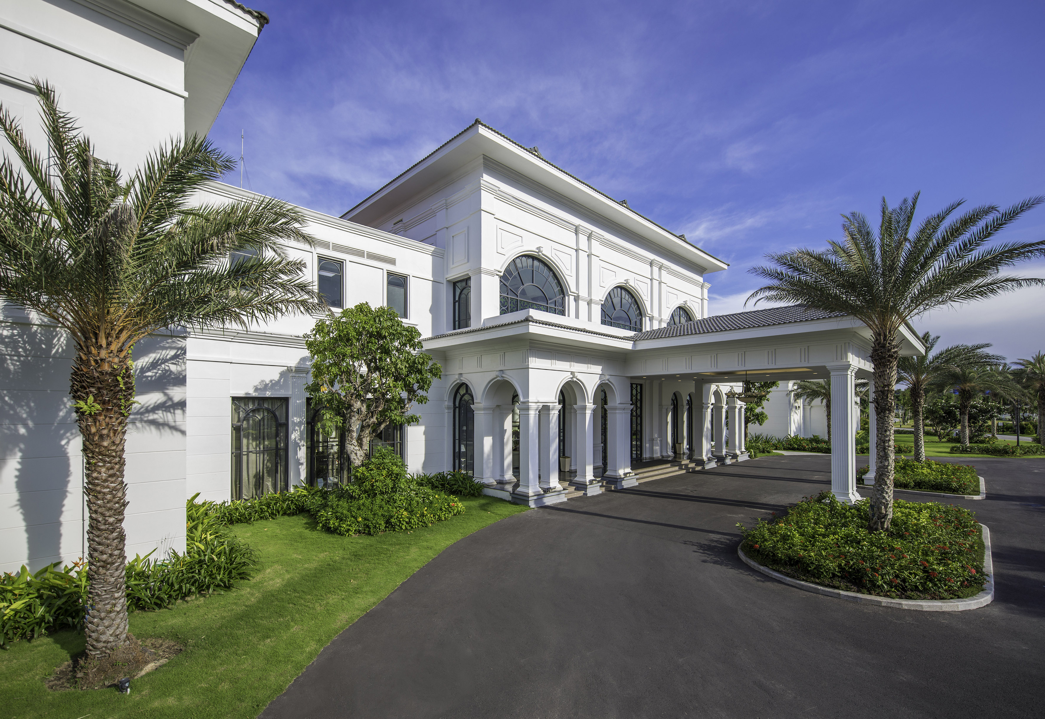 White luxury resort entrance with arched facade and palm trees.