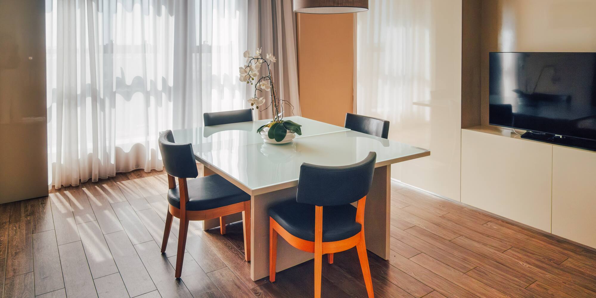 Contemporary dining area with glass table, dark chairs, and sheer curtains.