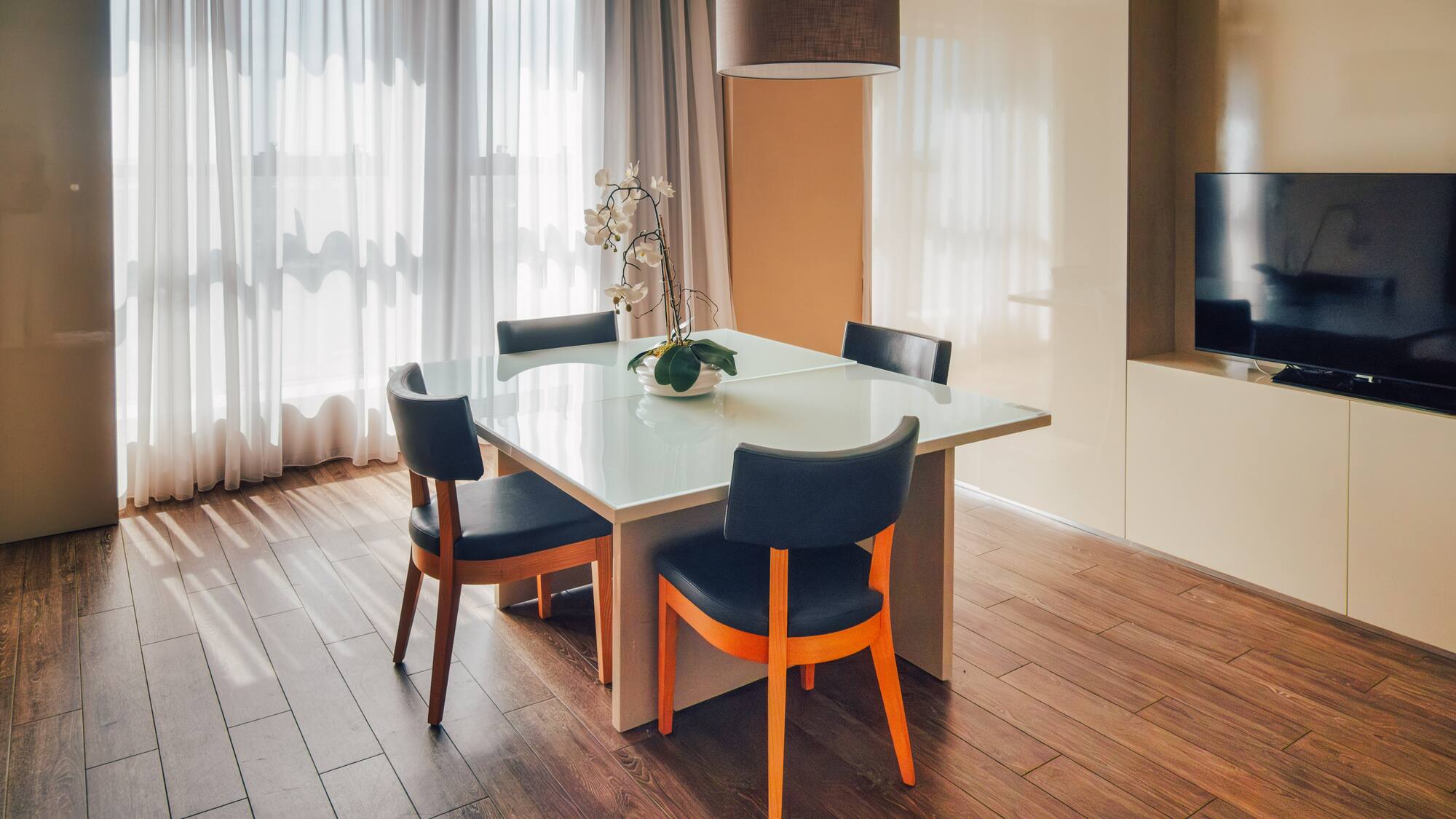 Contemporary dining area with glass table, dark chairs, and sheer curtains.