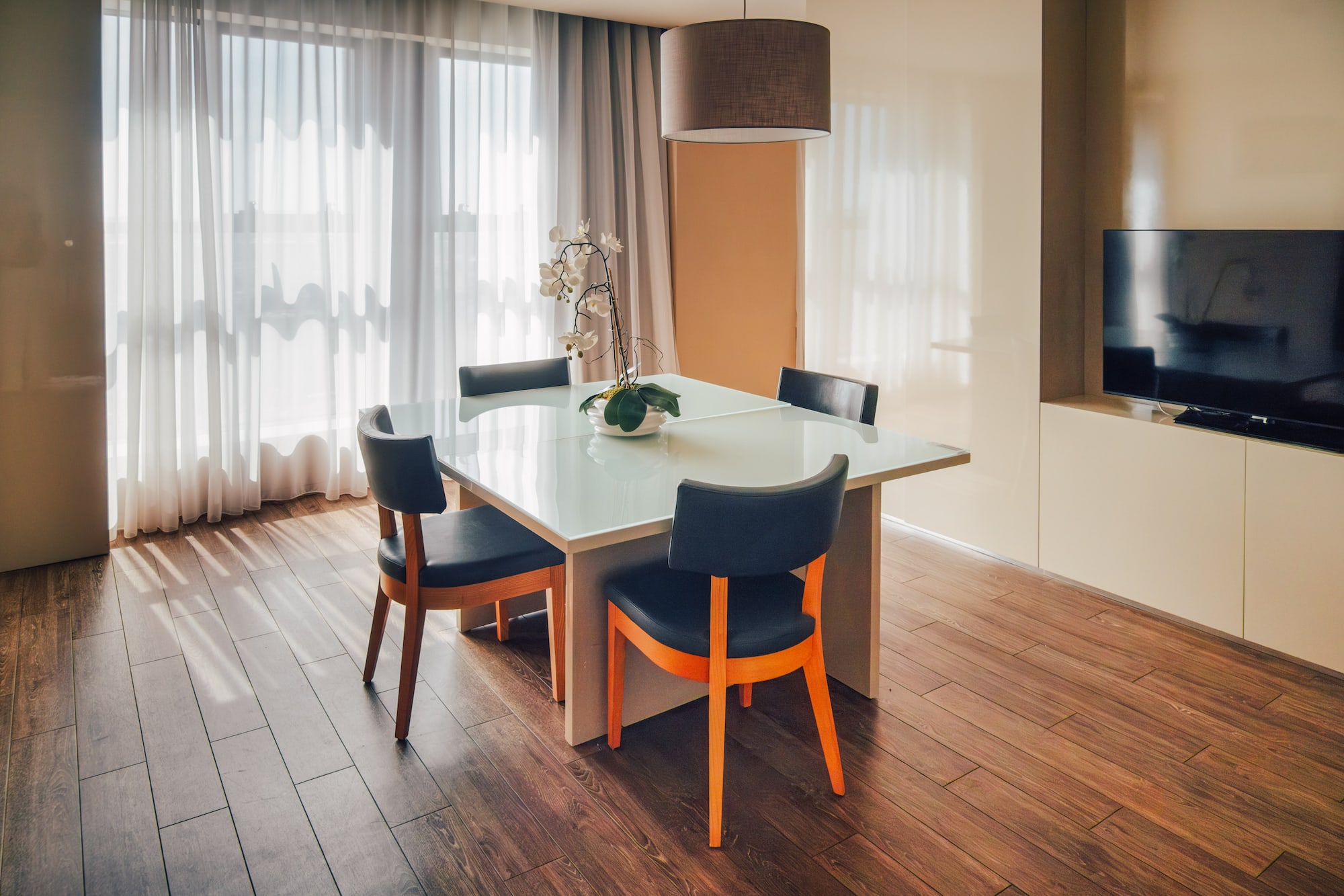 Contemporary dining area with glass table, dark chairs, and sheer curtains.
