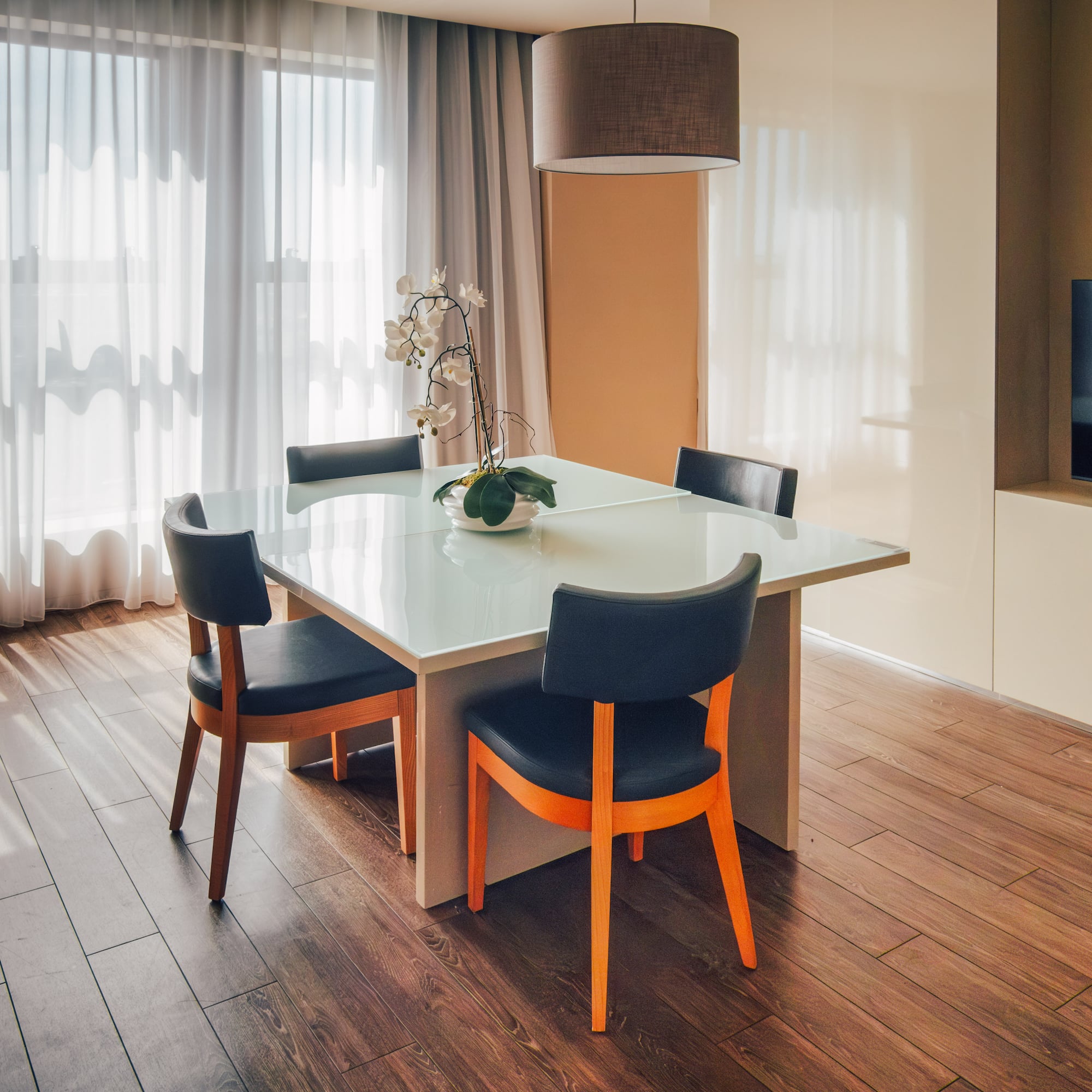 Contemporary dining area with glass table, dark chairs, and sheer curtains.