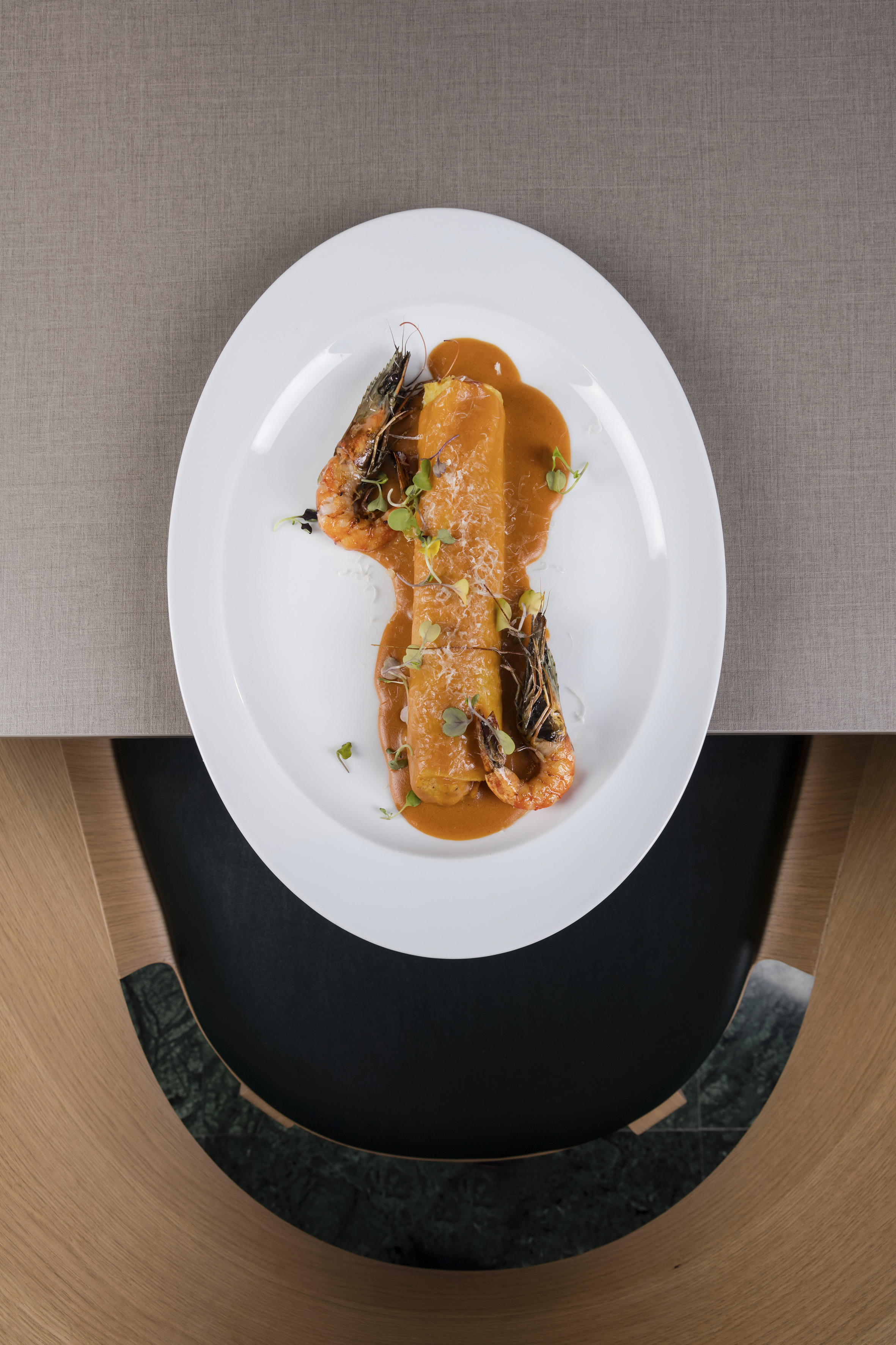 Seafood cannelloni with prawns, orange sauce, and microgreens.