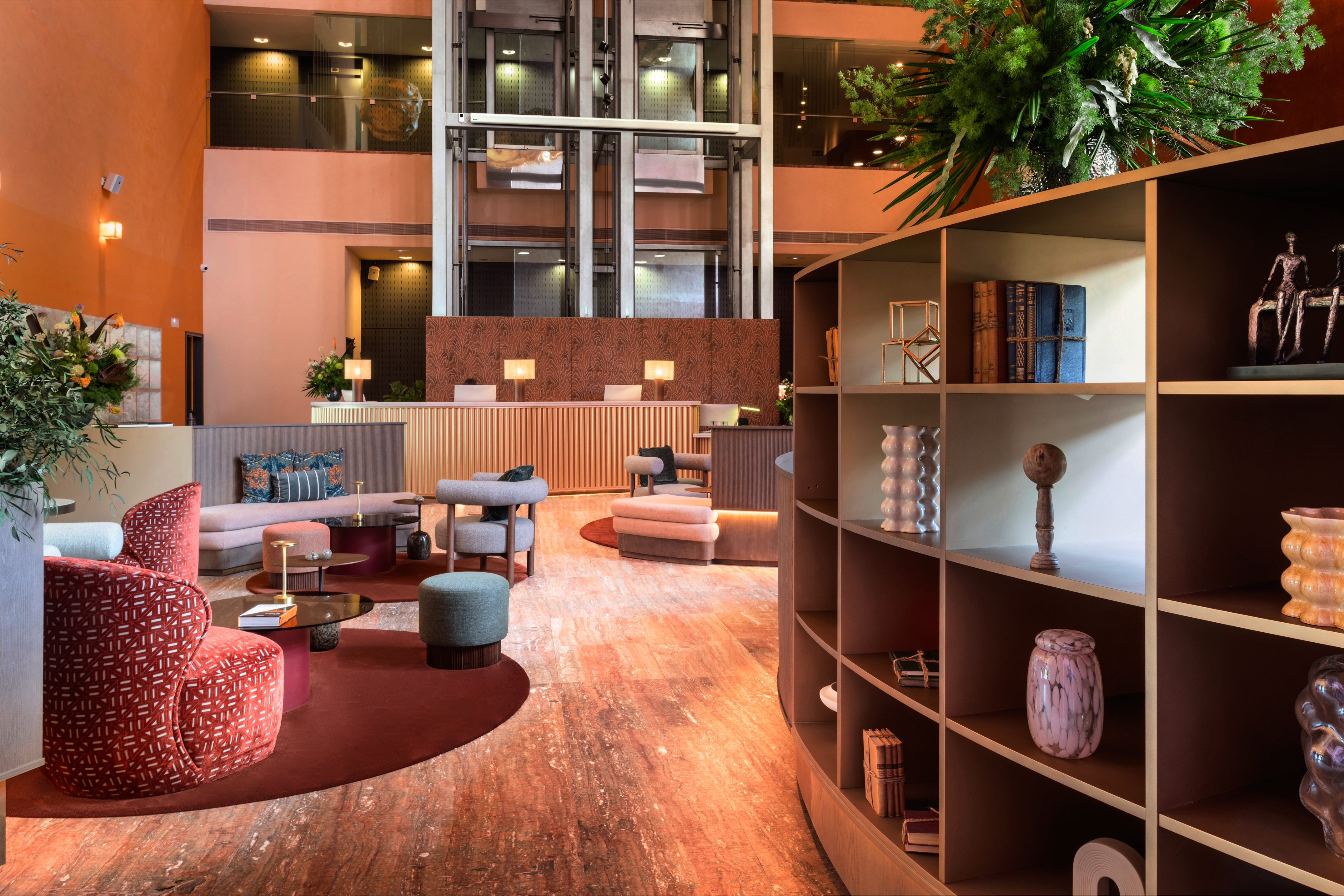 Modern hotel lobby: warm tones, lounge seating, reception, glass elevators.