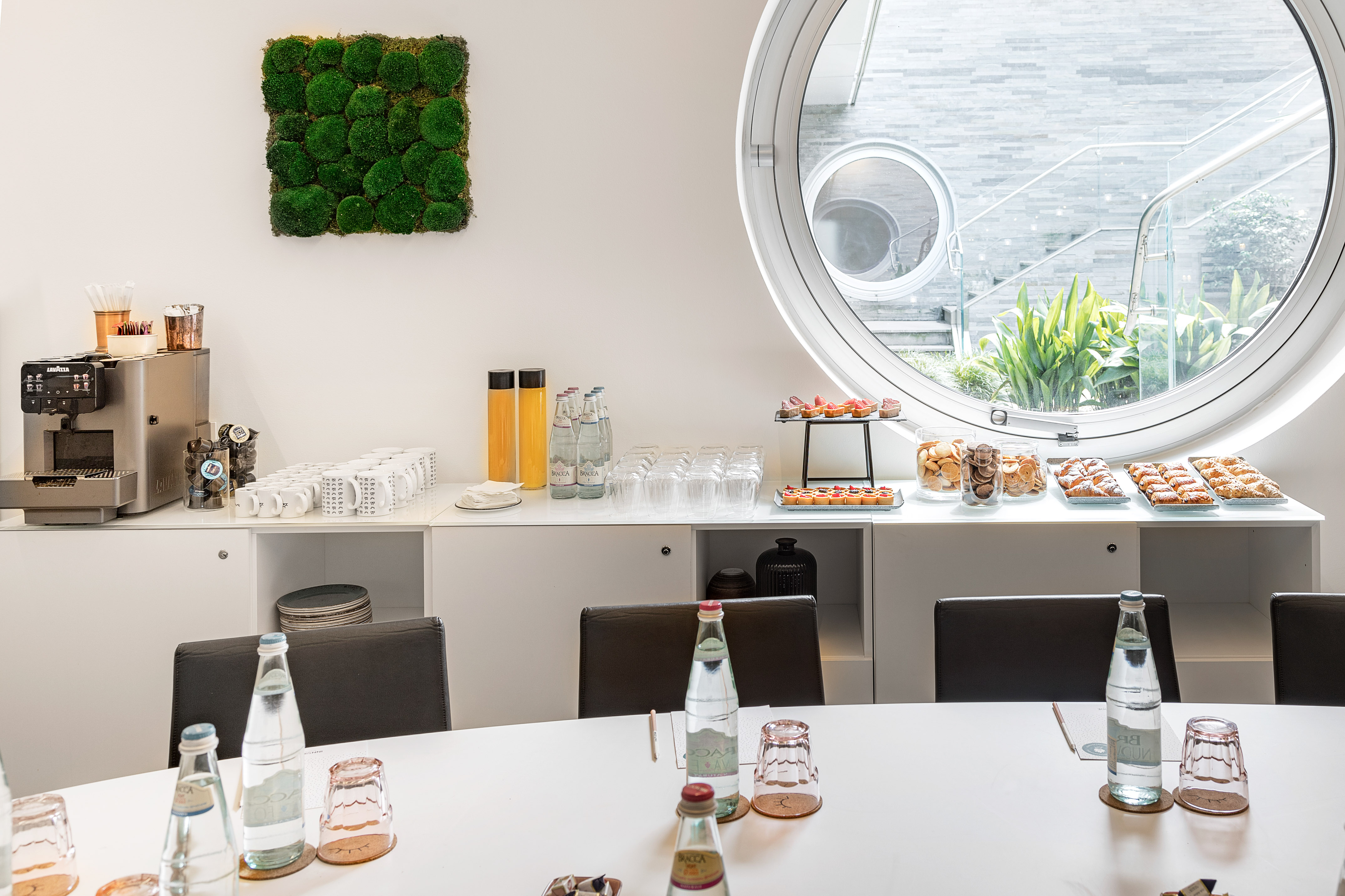 Modern meeting room with coffee, pastries, drinks, moss wall, round window.