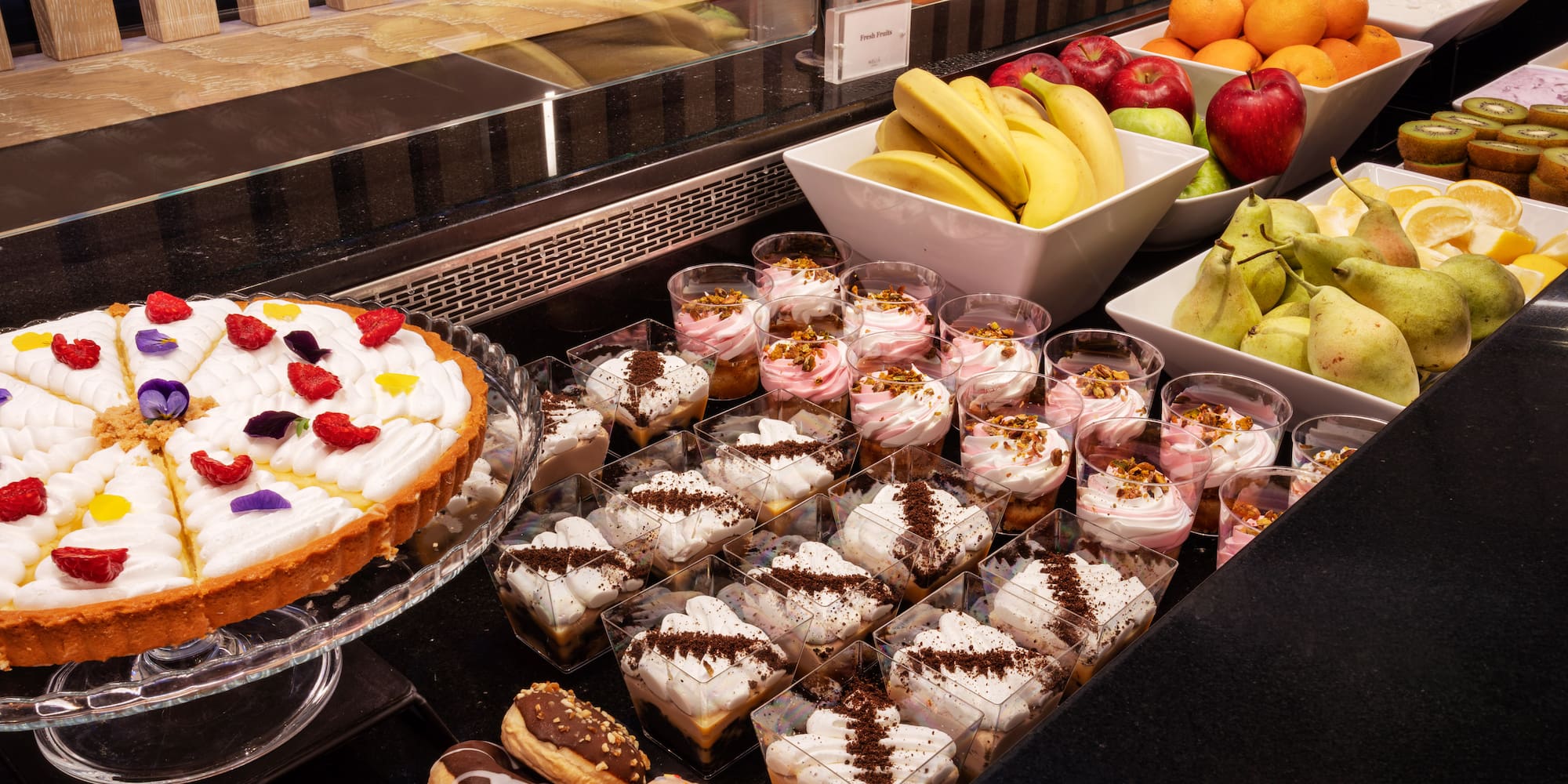 Extensive dessert and fresh fruit buffet: tart, donuts, individual cups, fresh fruit.