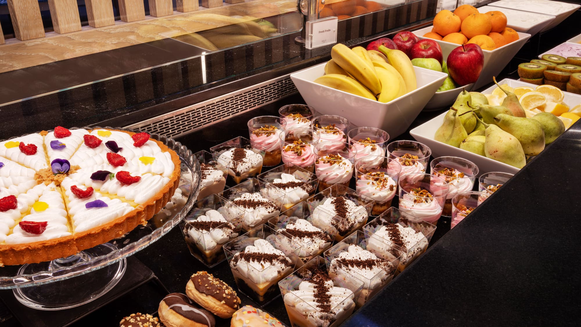 Extensive dessert and fresh fruit buffet: tart, donuts, individual cups, fresh fruit.