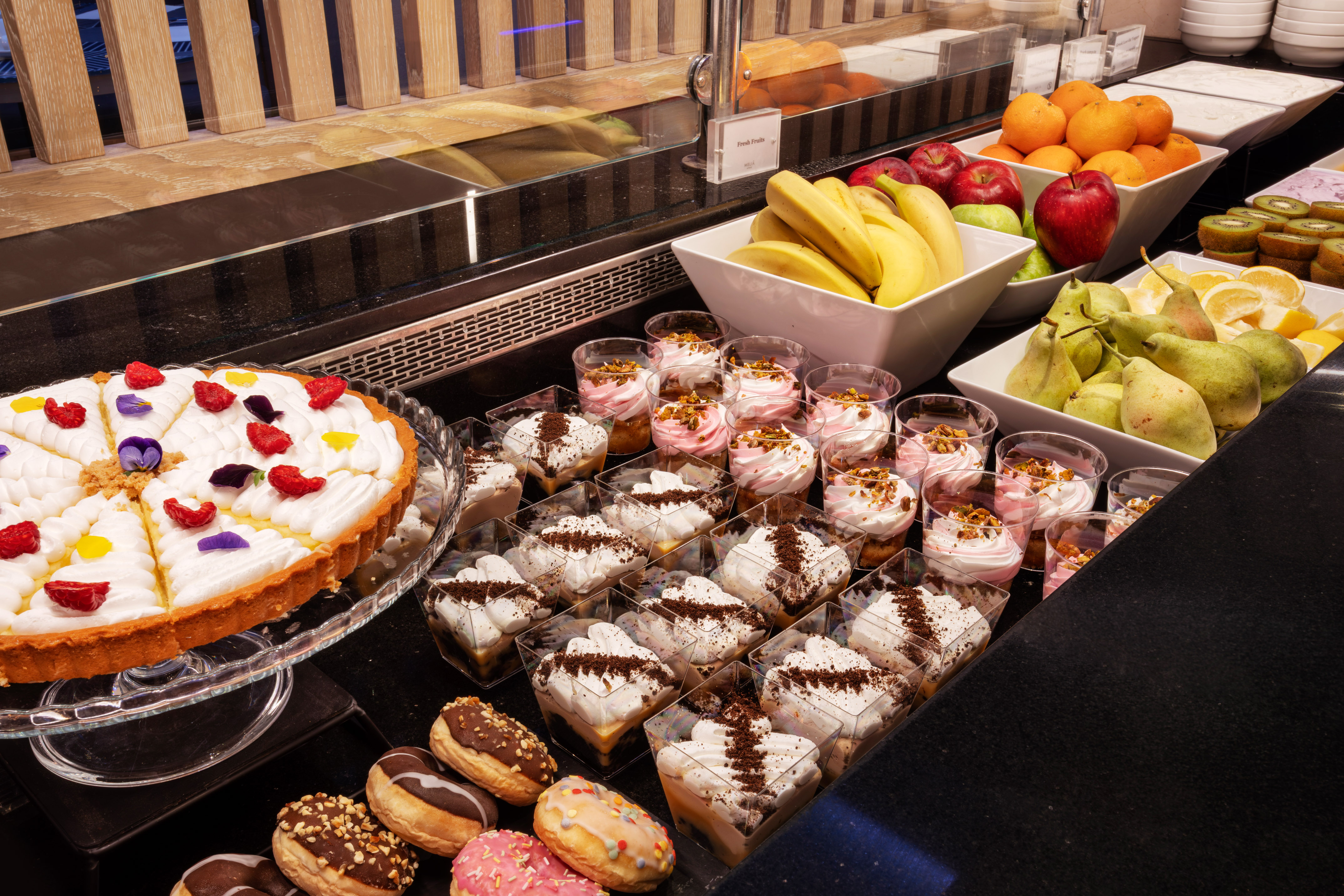Extensive dessert and fresh fruit buffet: tart, donuts, individual cups, fresh fruit.