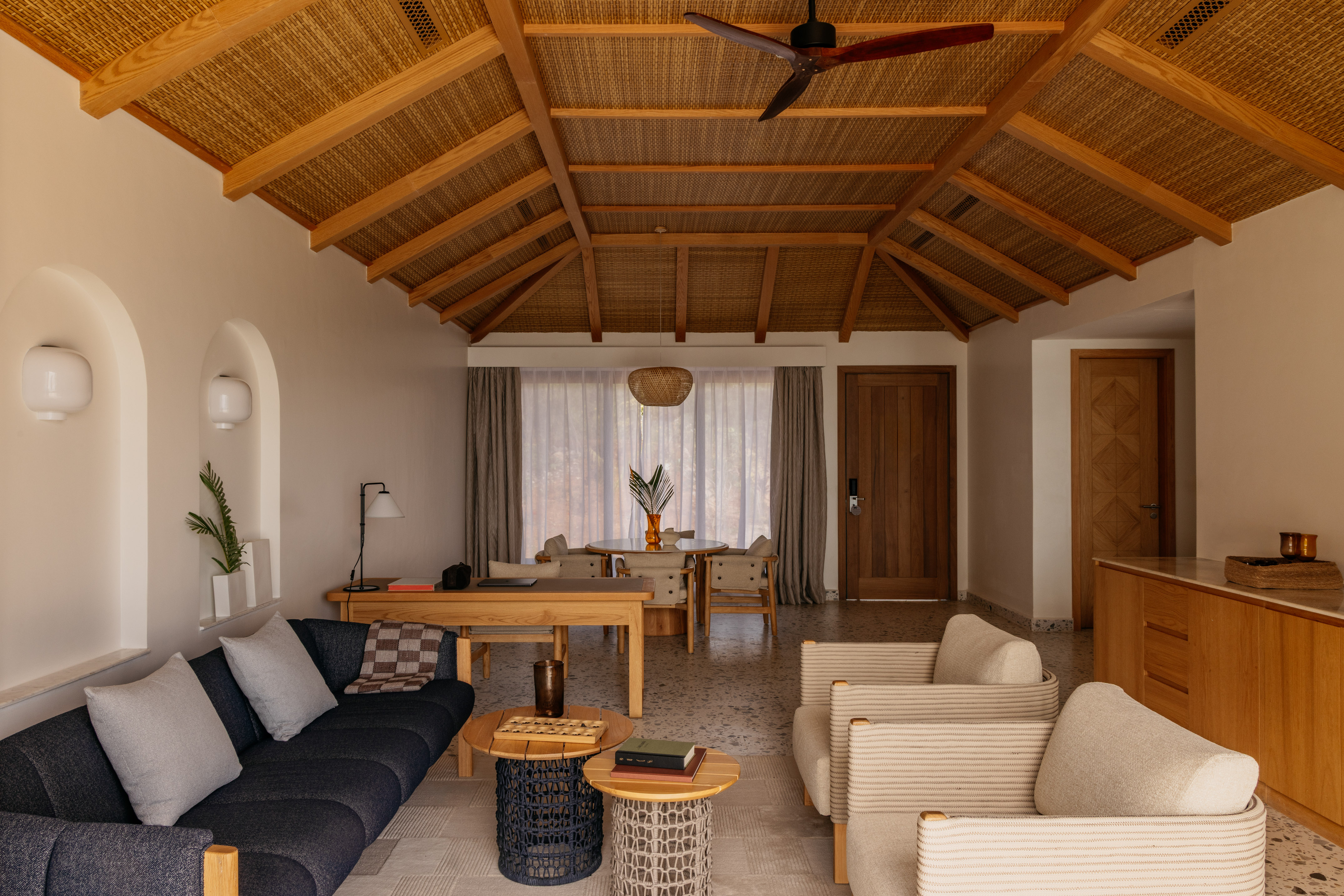 Modern tropical living room with woven ceiling, dark sofa, and light armchairs.