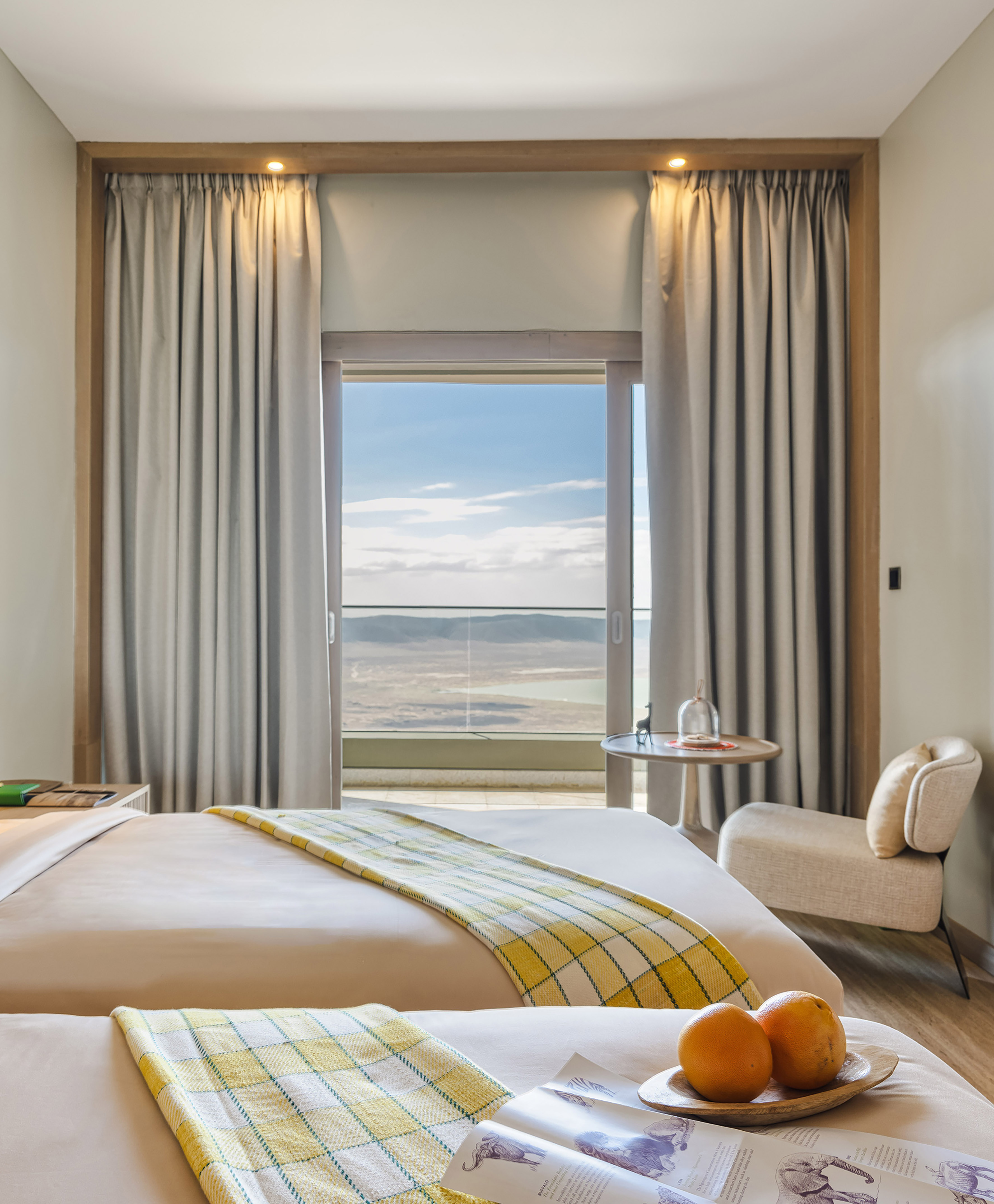 Contemporary hotel bedroom with lake view, safari magazine, and oranges.