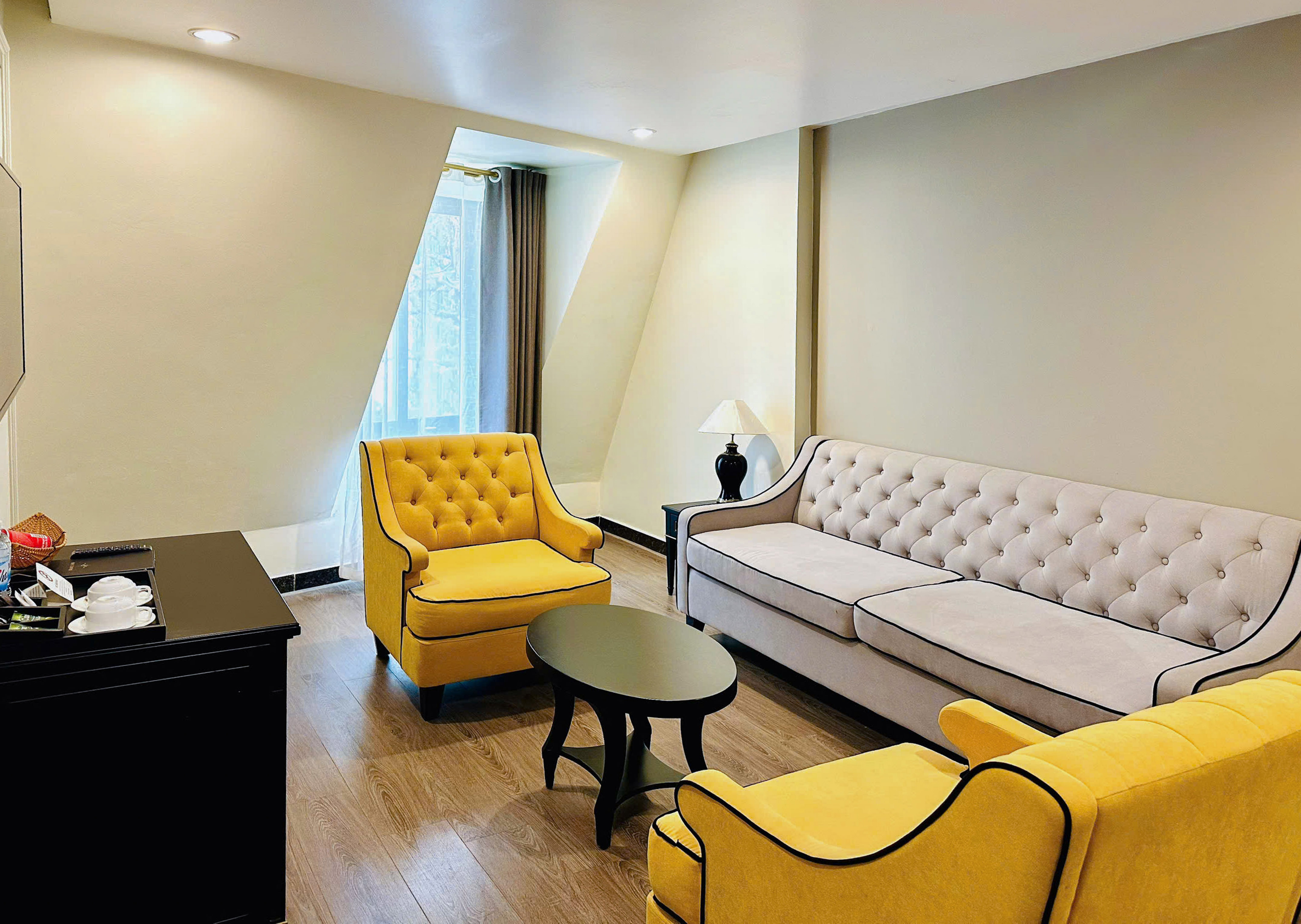 Living room with tufted beige sofa, yellow armchairs, black coffee table, and wood floor. - Executive Suite - Hotel Sapa Square Affiliated by Meliá, Sapa