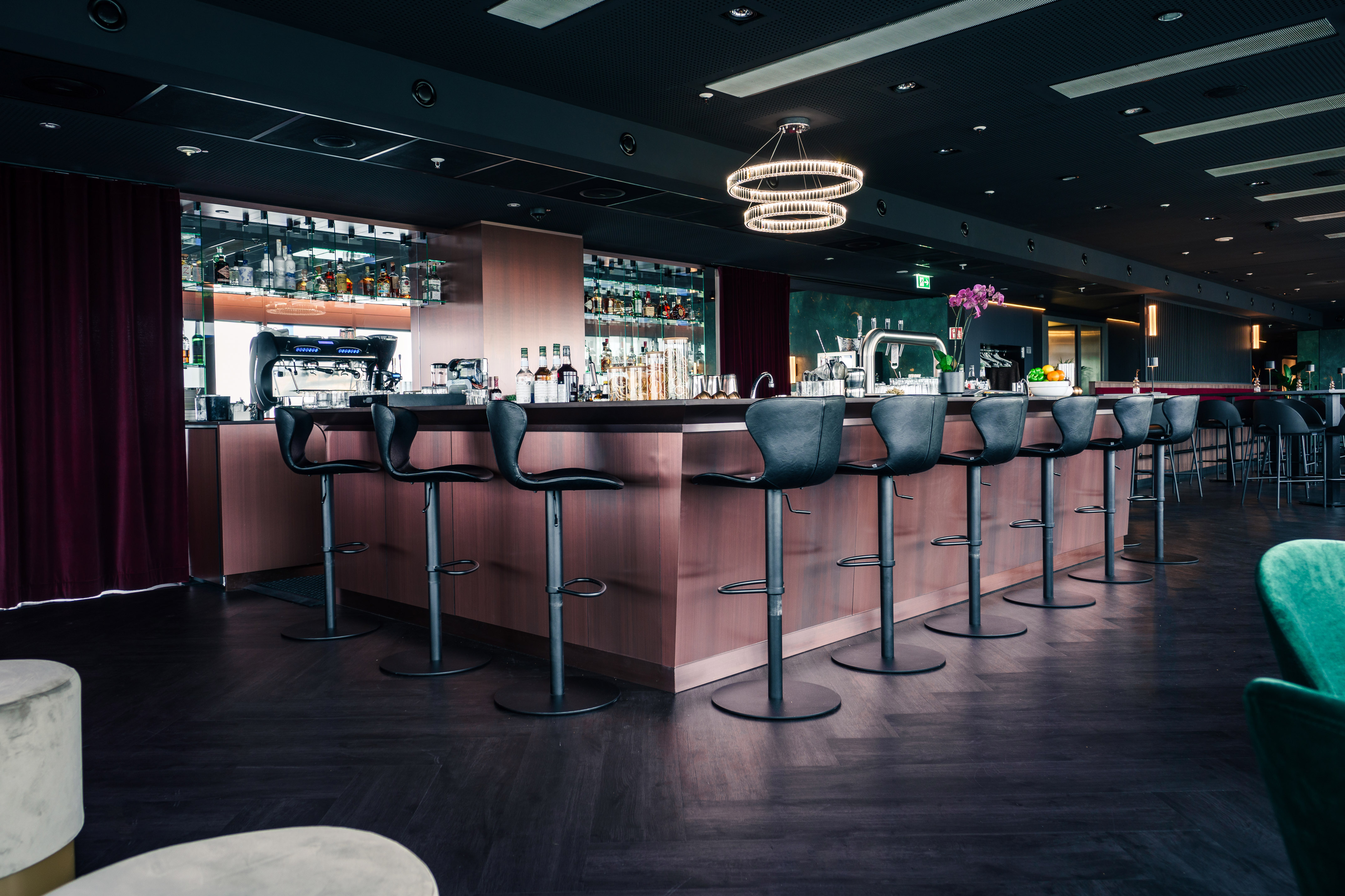 Modern bar lounge with black stools, dark wooden counter, and liquor display.