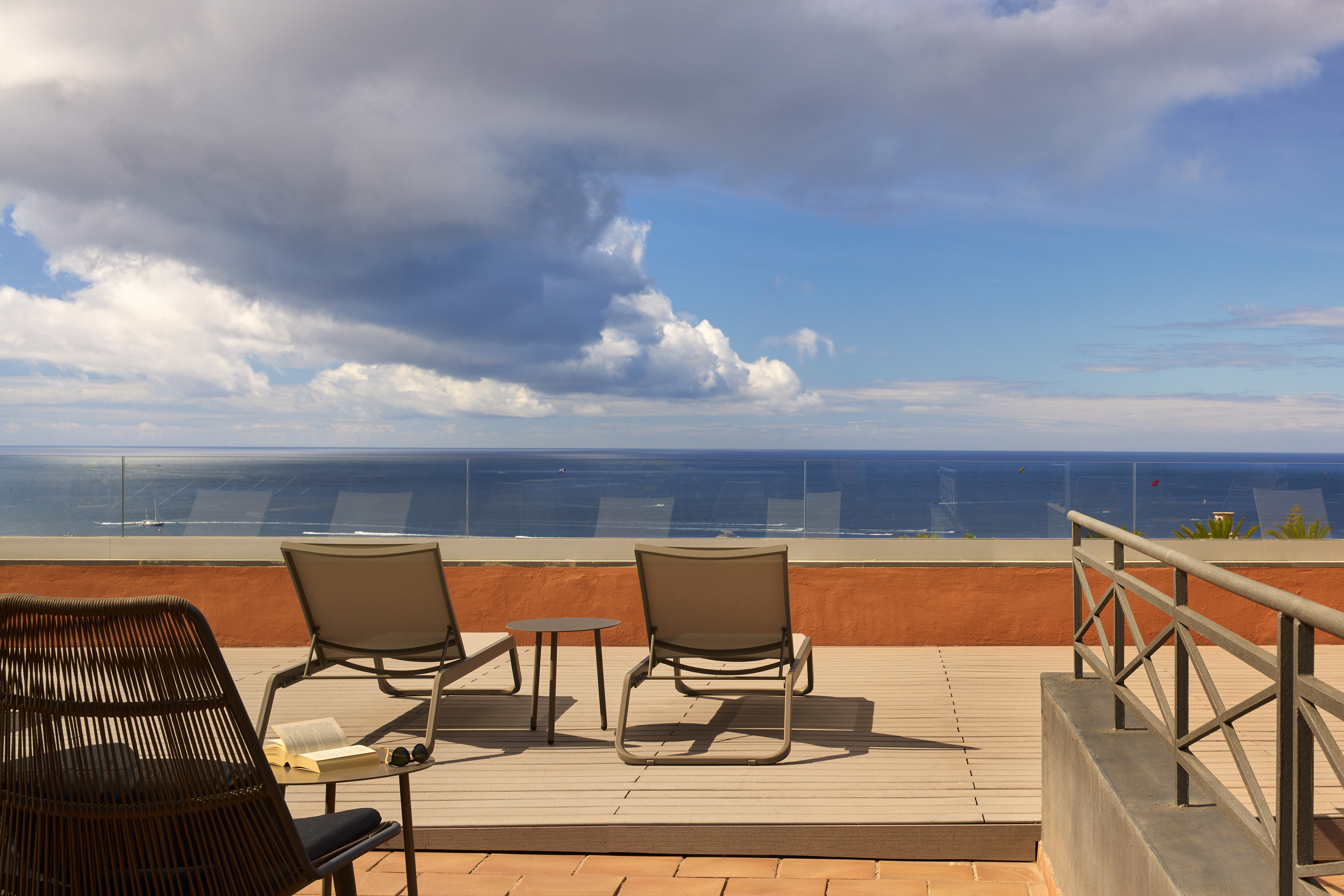 Ocean view balcony with lounge chairs, glass railing, and partly cloudy sky.