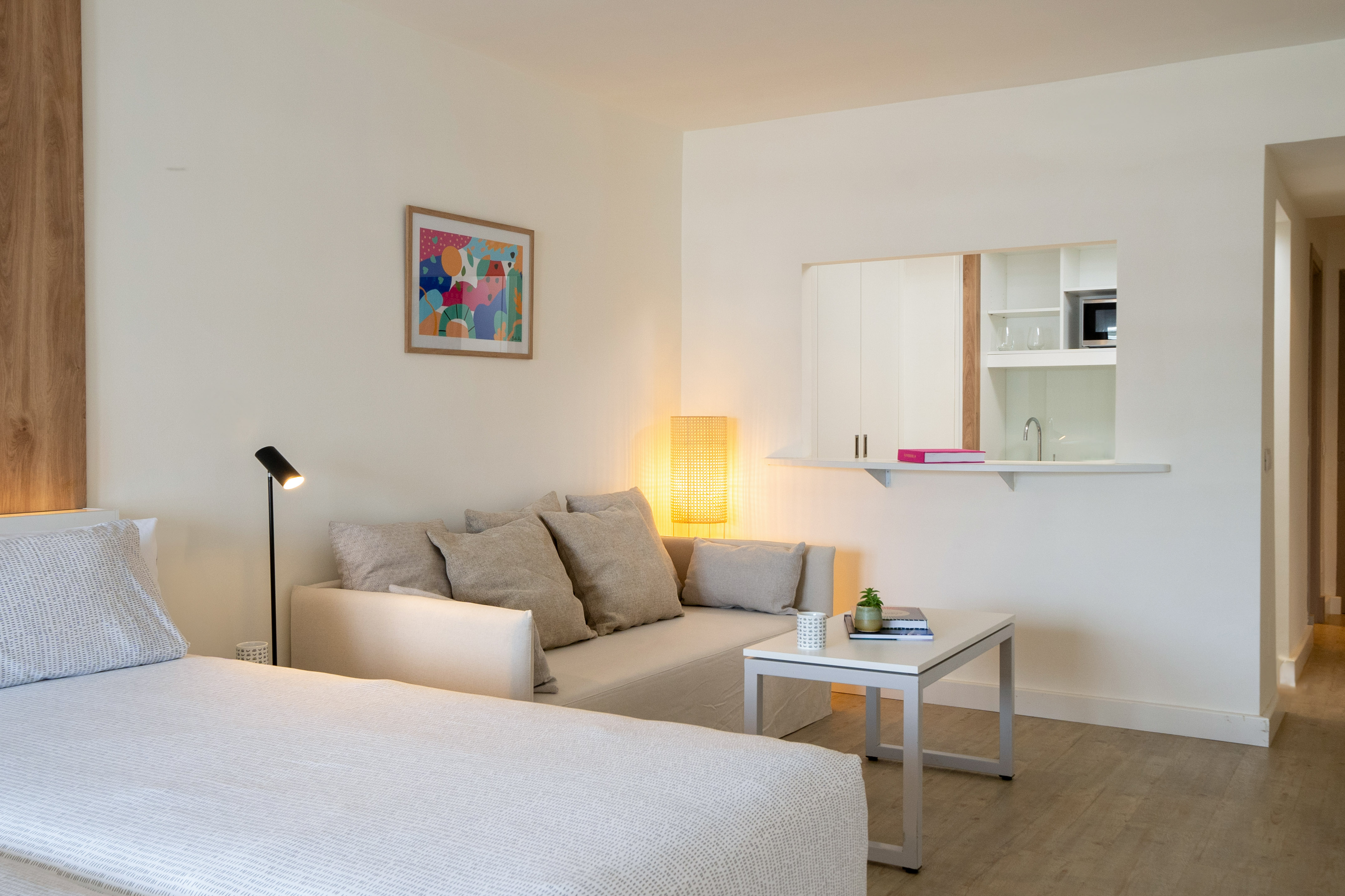 Modern minimalist studio apartment with bed, sofa, and kitchenette.