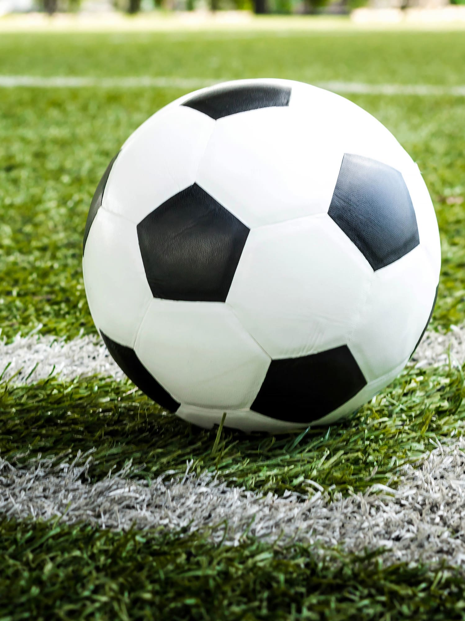 Black and white soccer ball on a green football field, near the white line.