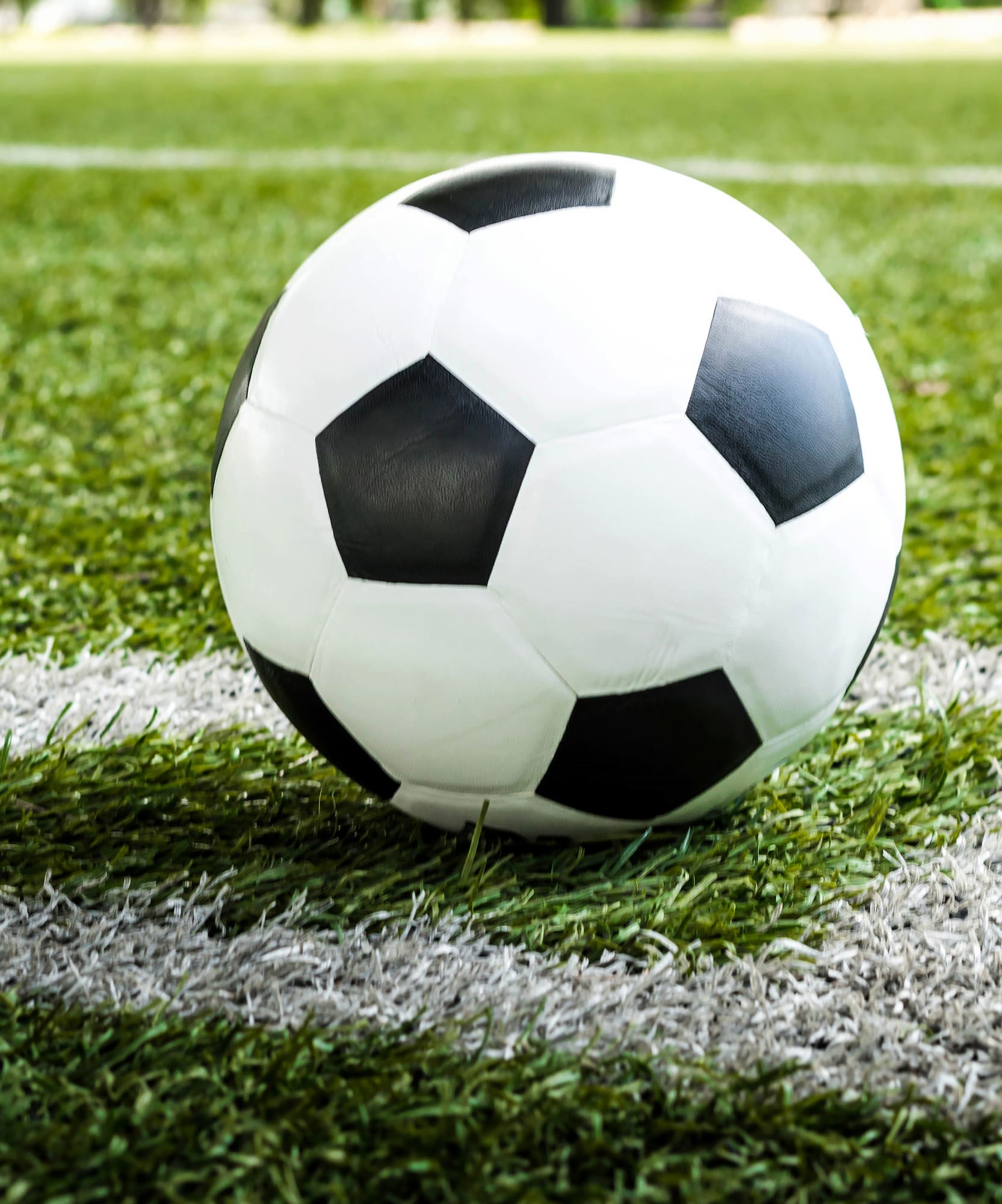 Black and white soccer ball on a green football field, near the white line.