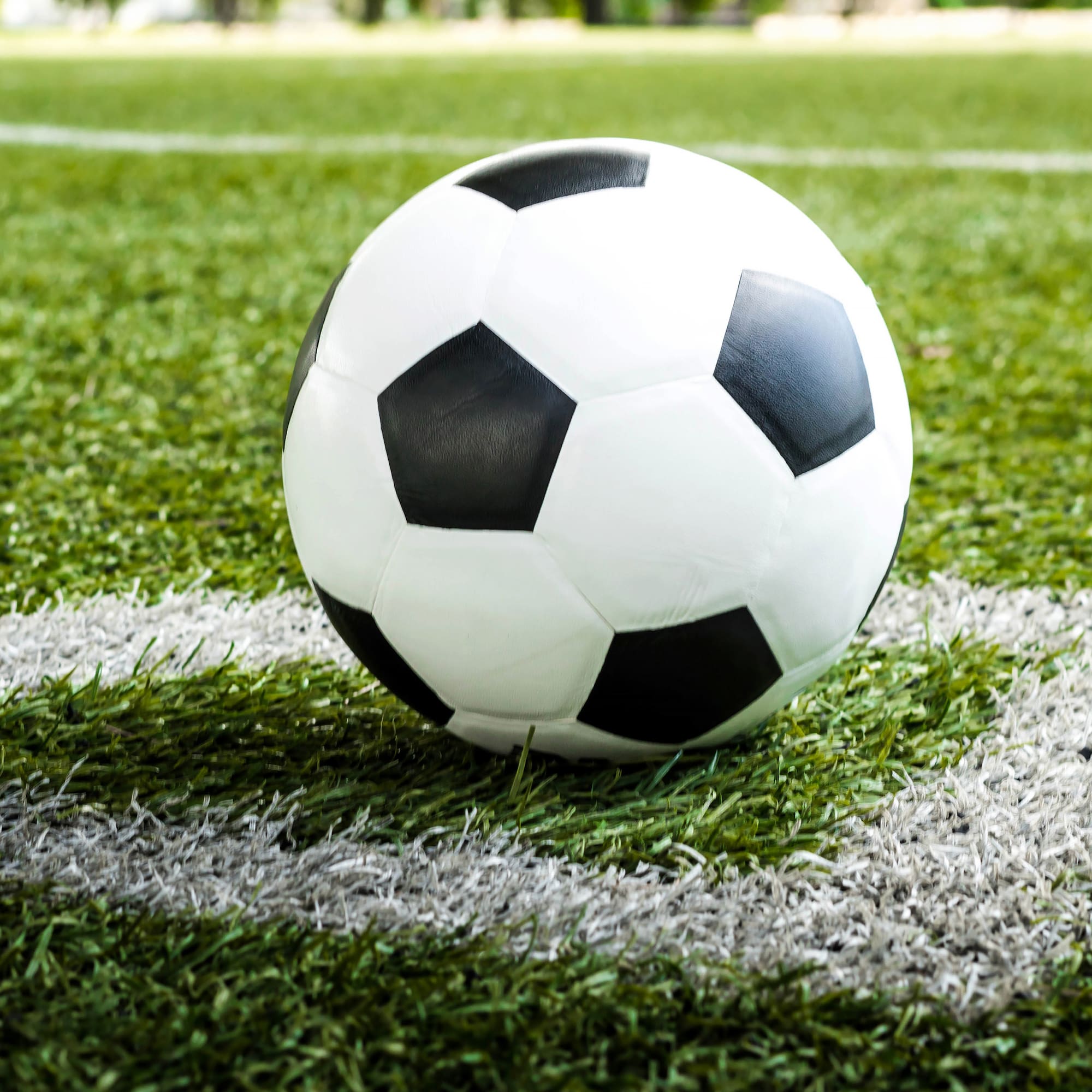 Black and white soccer ball on a green football field, near the white line.