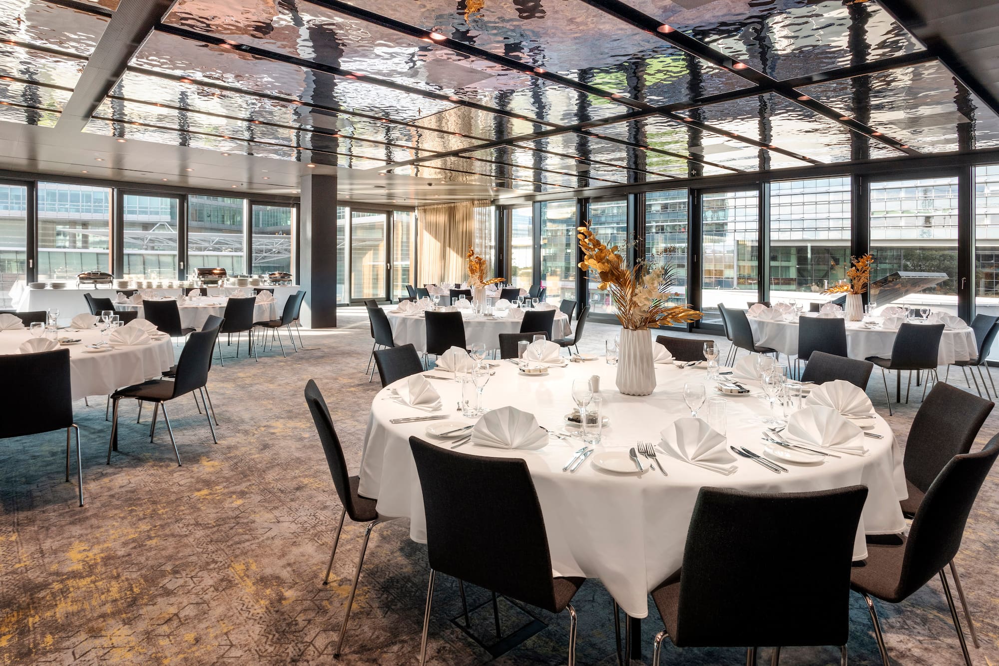 Modern event hall with set round tables, black chairs, and unique ceiling.