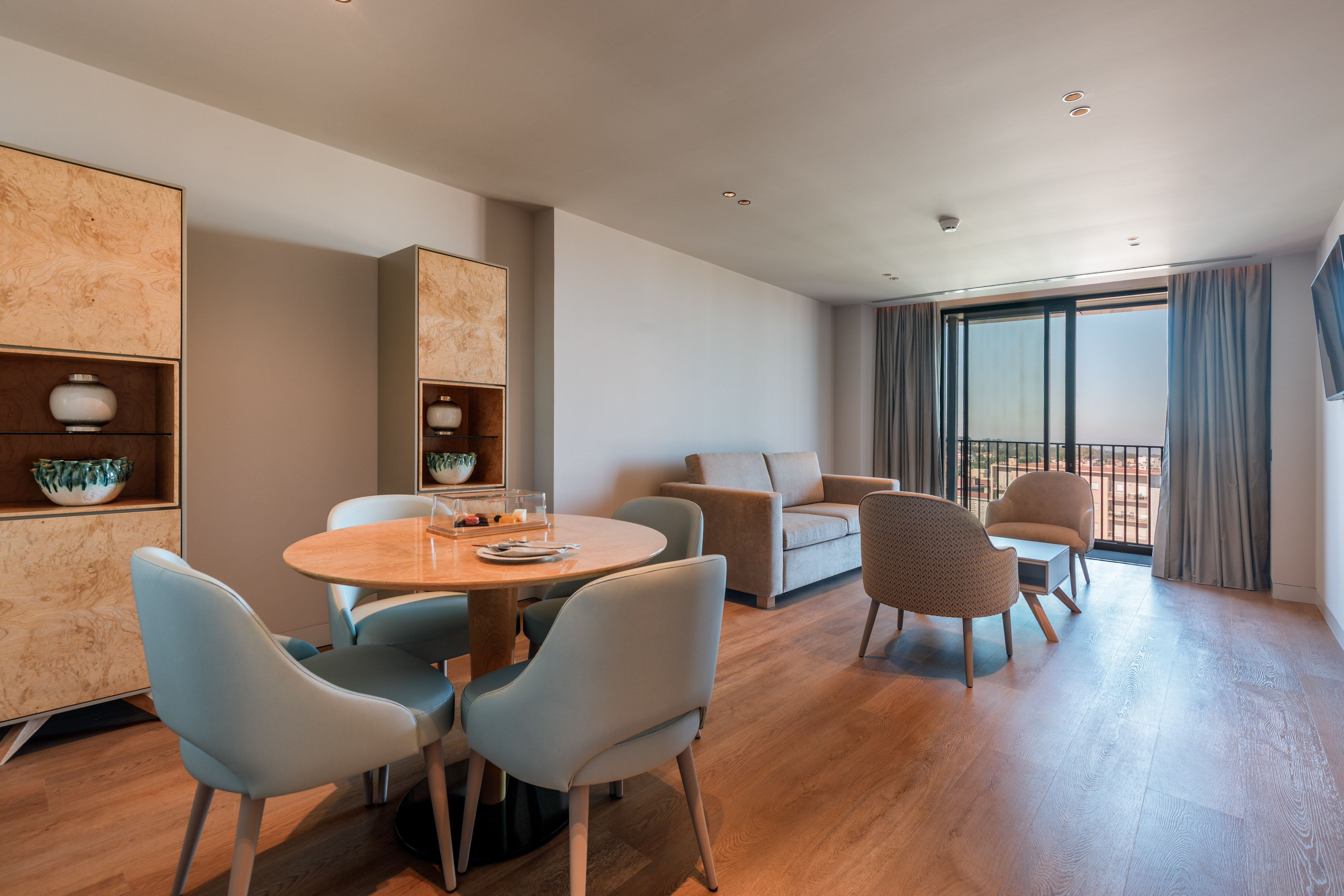 Stylish hotel suite with modern dining, living area, and balcony city view.