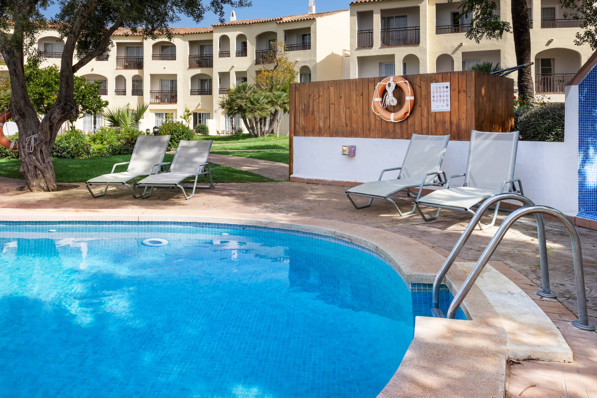 Outdoor resort pool area with blue water, sun loungers, and hotel building.