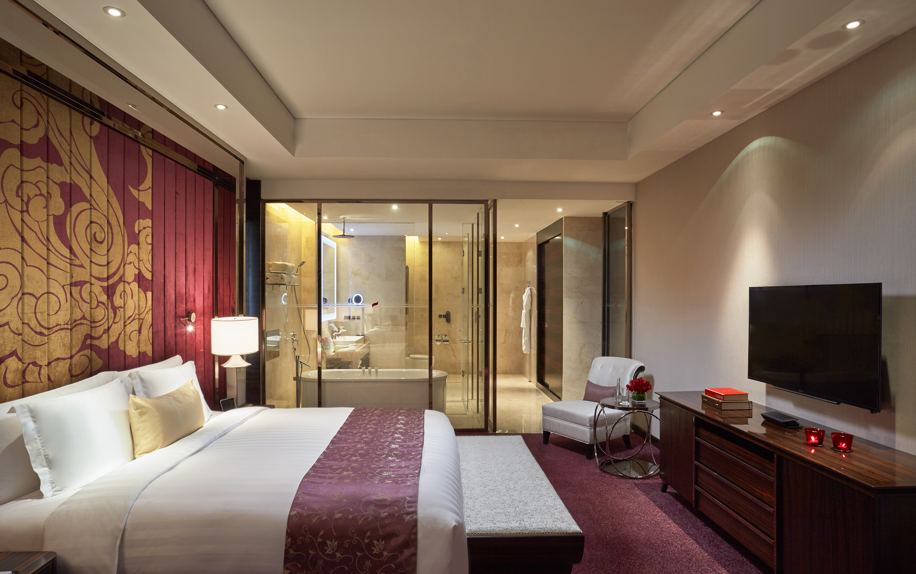 Elegant hotel room with king bed, red accents, and open glass bathroom.