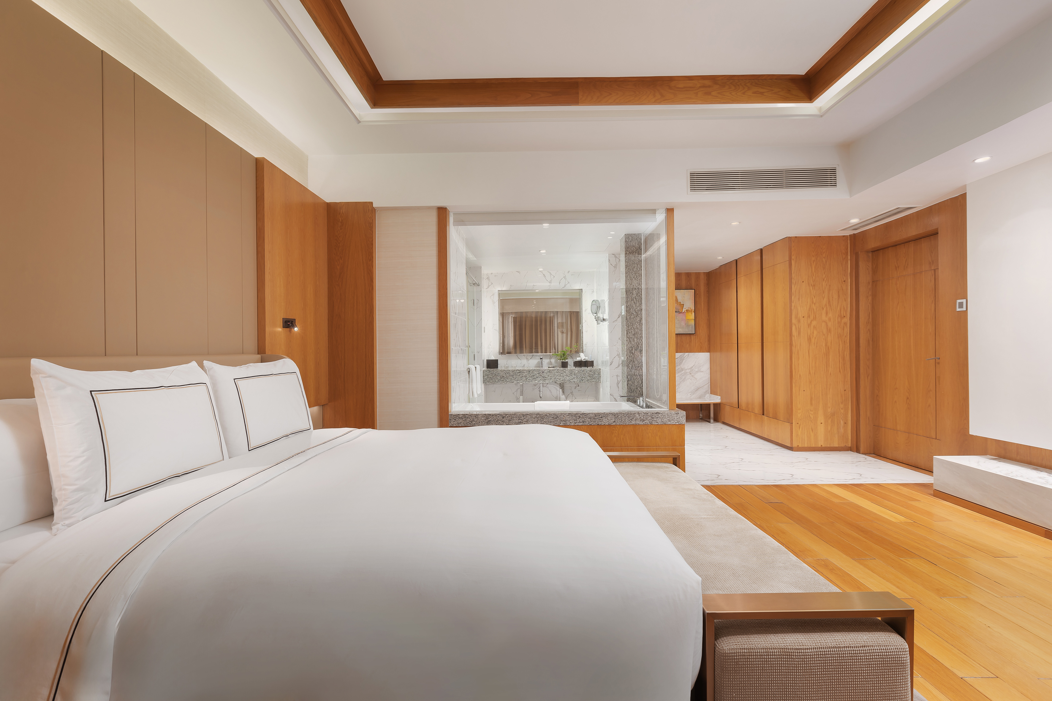 Modern hotel bedroom with white bed, wood accents, and open-plan bathroom.