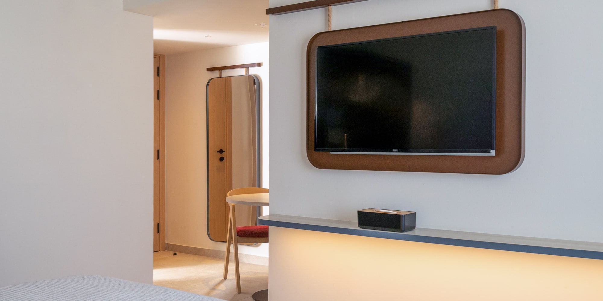 Modern hotel room with wall-mounted TV, brown frame, and illuminated shelf.