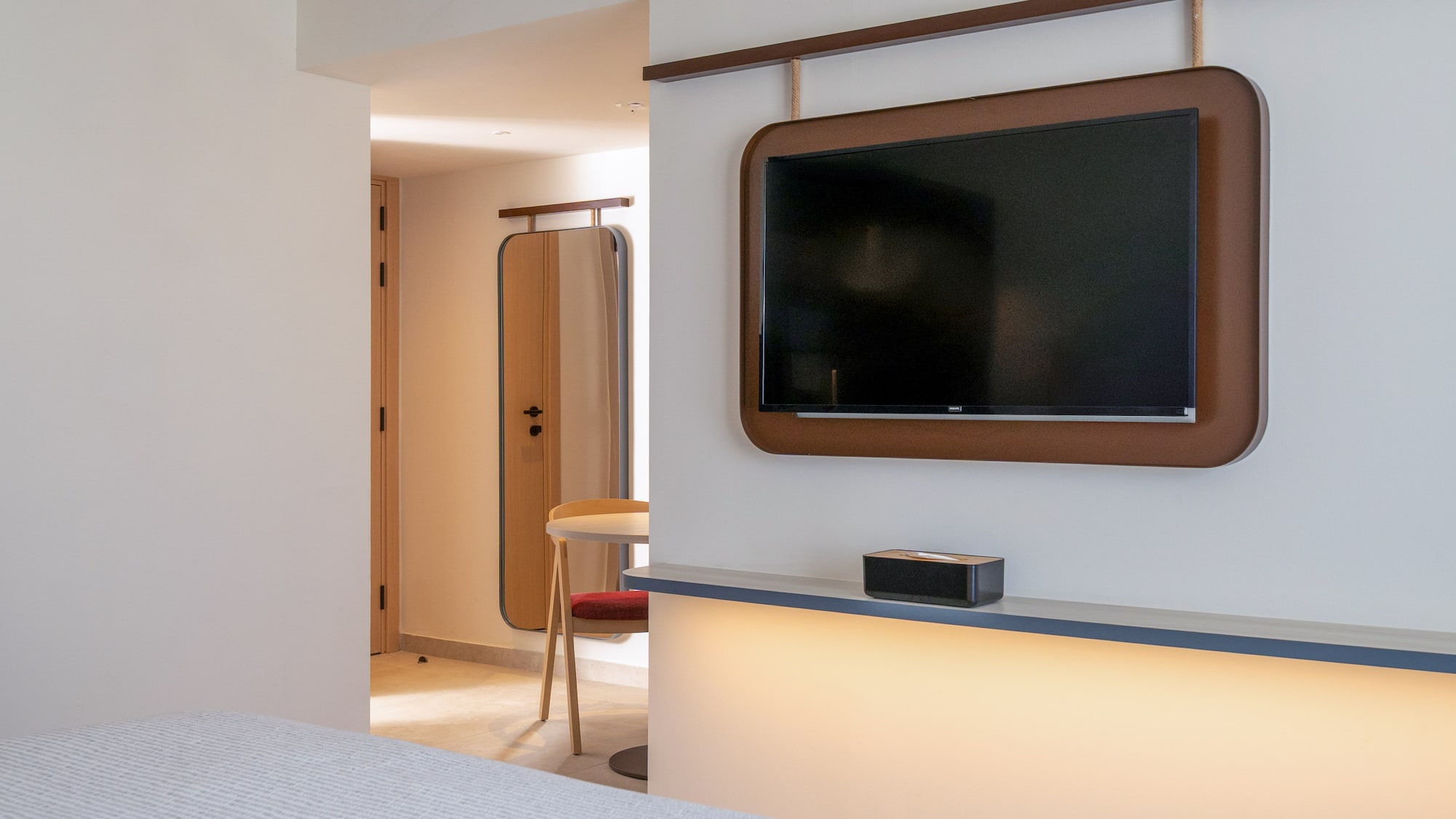 Modern hotel room with wall-mounted TV, brown frame, and illuminated shelf.