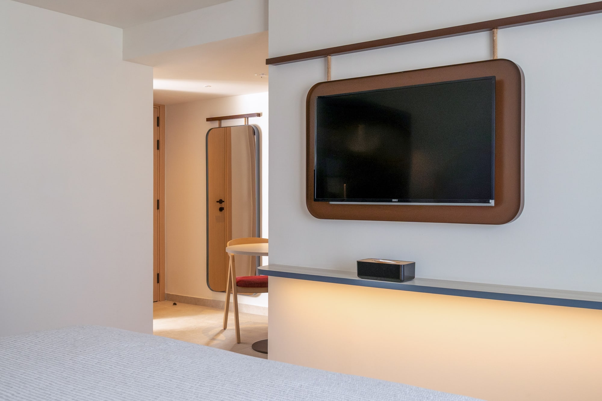 Modern hotel room with wall-mounted TV, brown frame, and illuminated shelf.